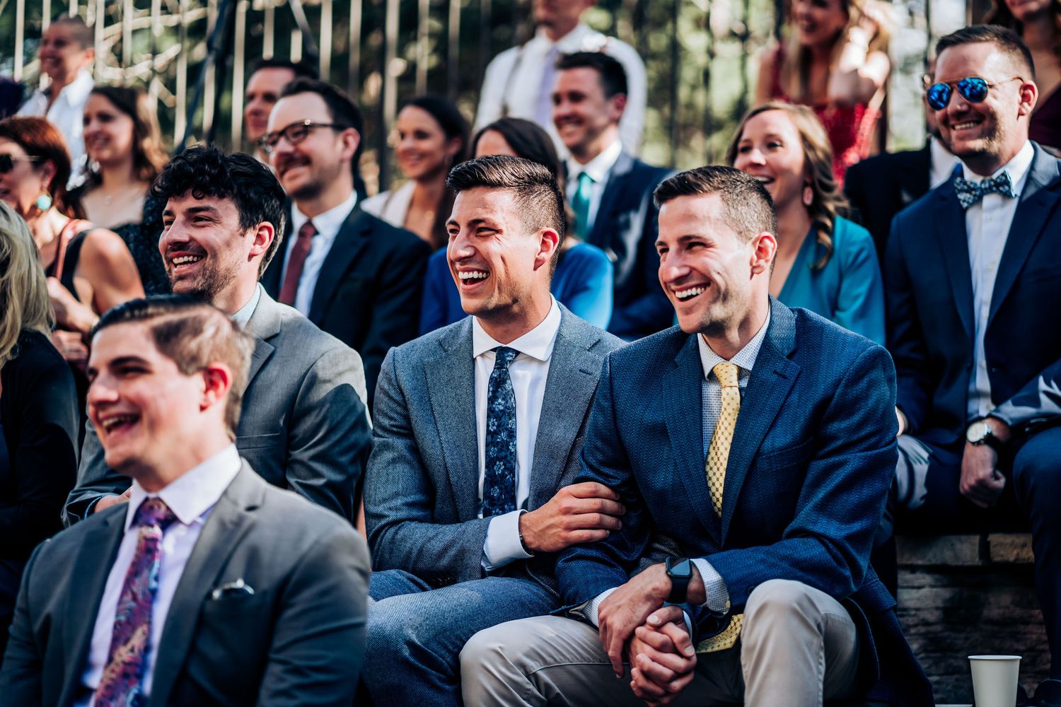 Wedding guests sharing joyful reactions during outdoor ceremony.