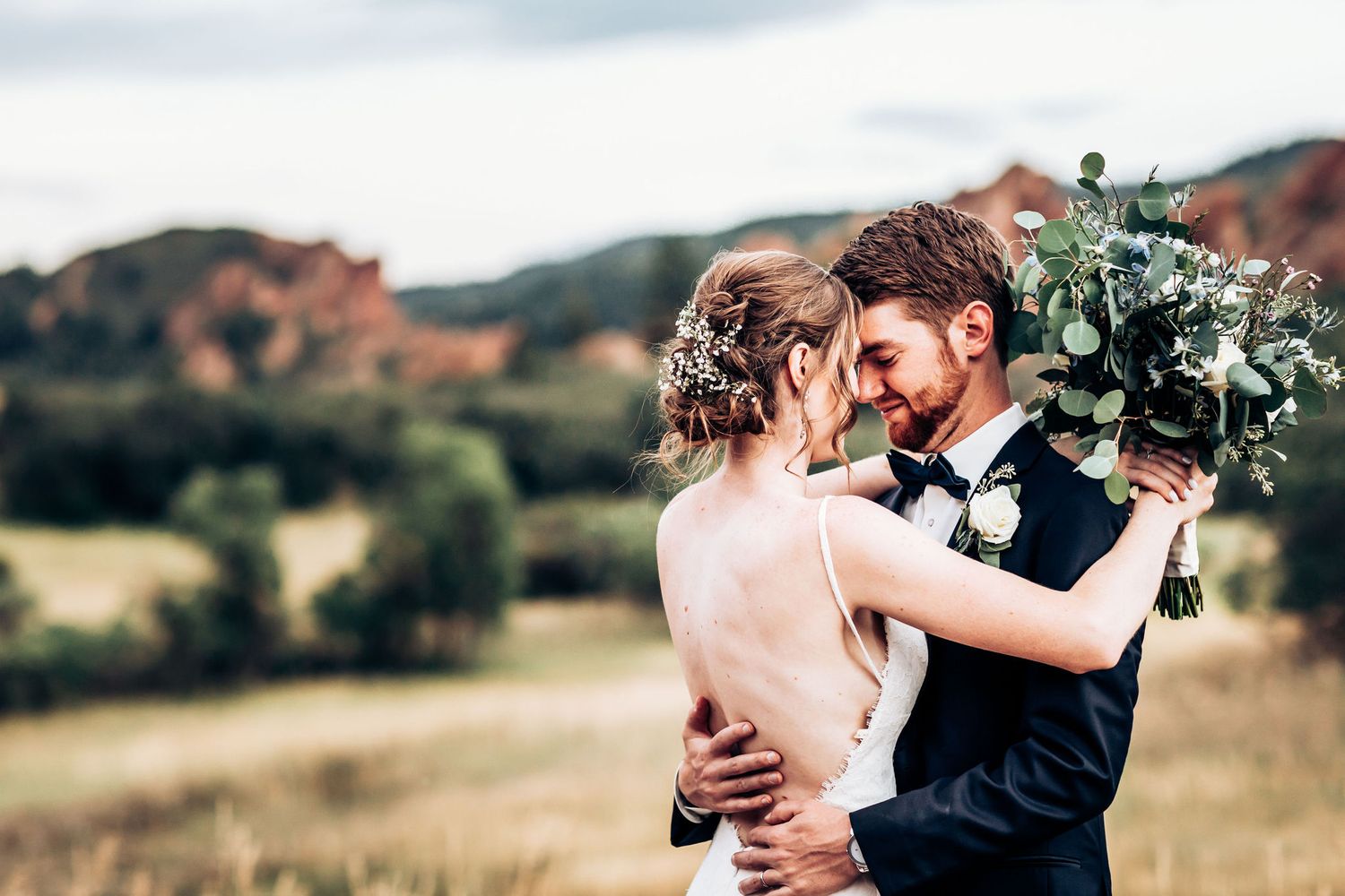 Intimate wedding portrait with lush greenery bouquet against mountain backdrop.