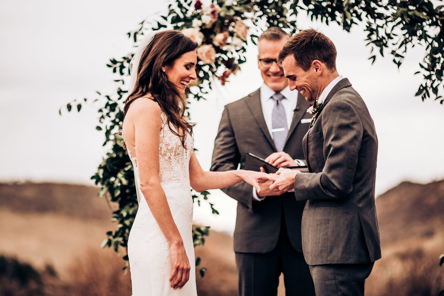 Intimate moment during ring exchange at outdoor wedding ceremony with mountain backdrop.