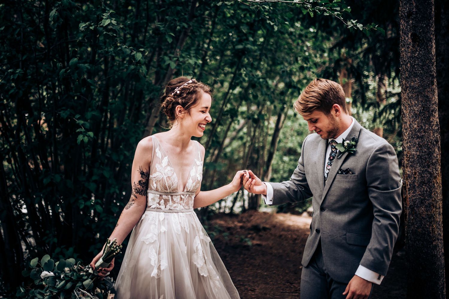 Candid moment of bride and groom holding hands while walking through forest path.