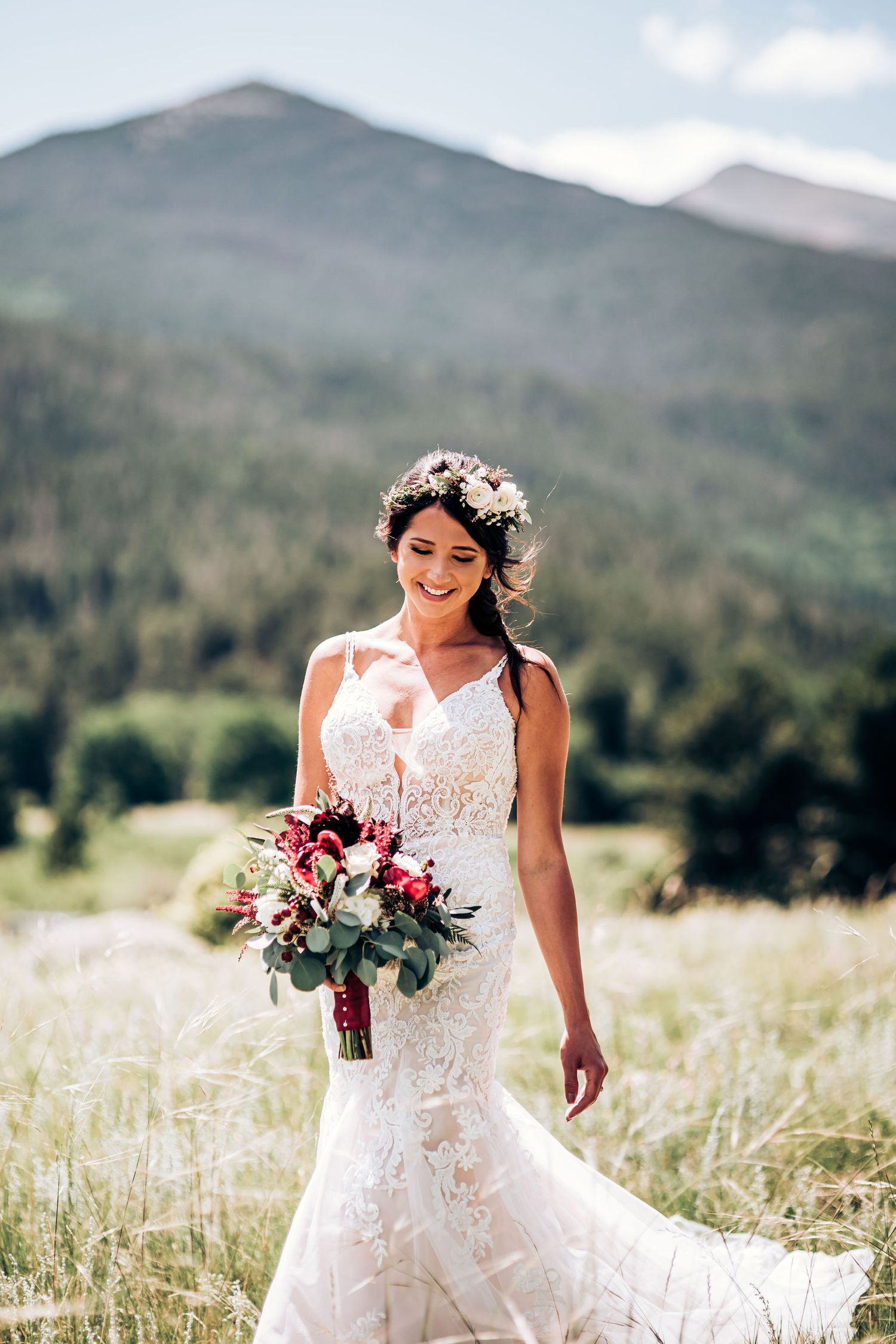 A sunlit wedding portrait featuring a delicate lace gown and vibrant bouquet against mountain peaks.