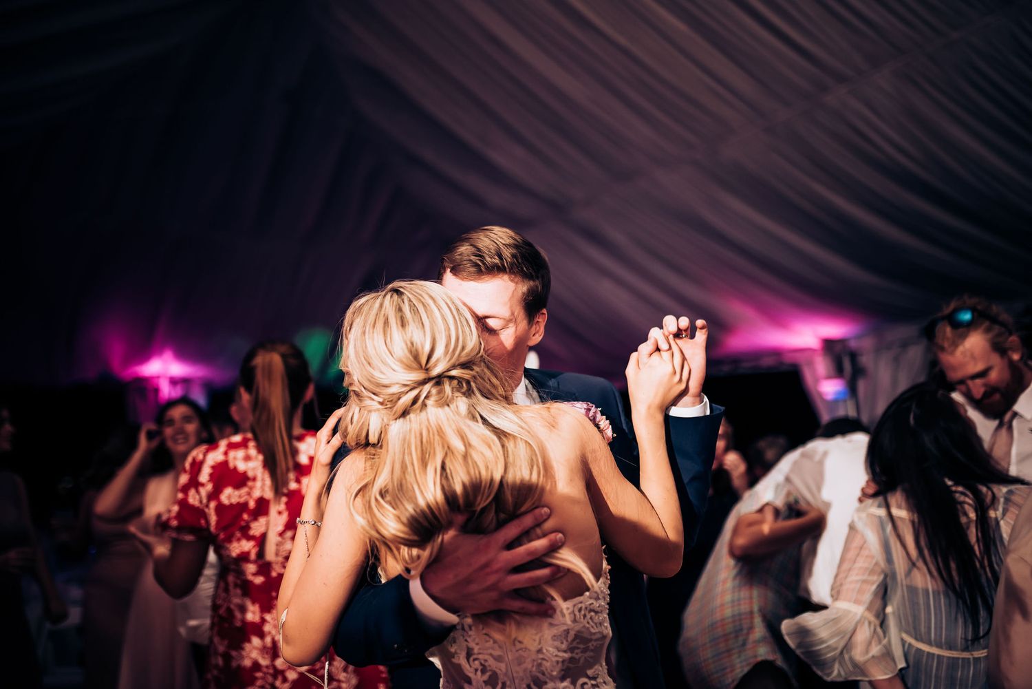 Couples slow dancing together at an evening wedding reception with purple lighting.