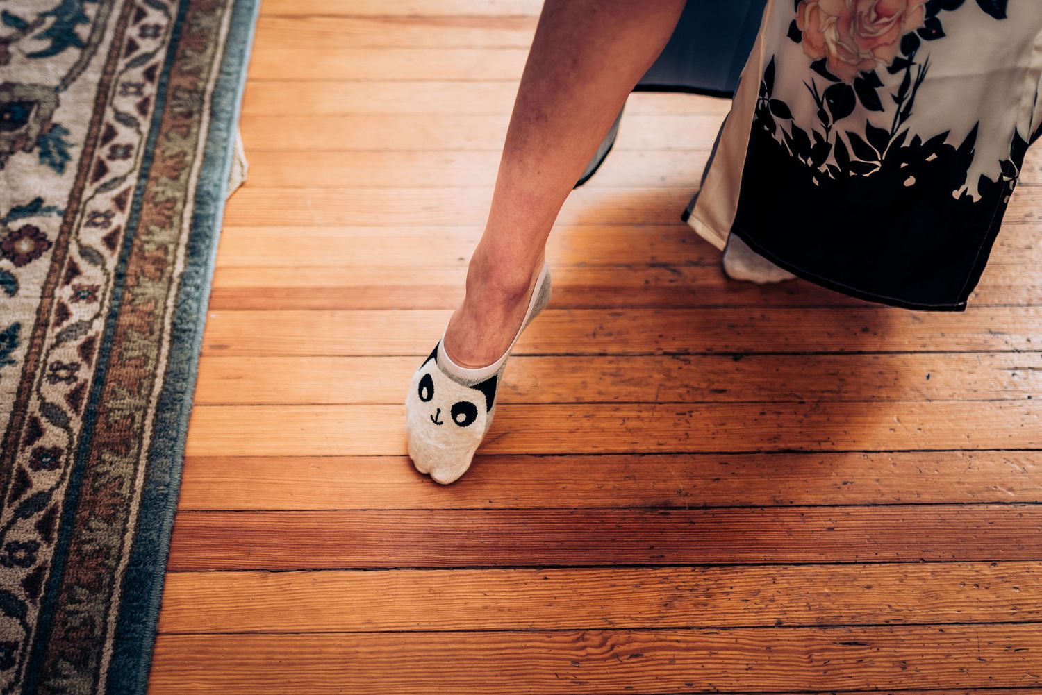 White panda slippers on hardwood floor next to decorative rug.