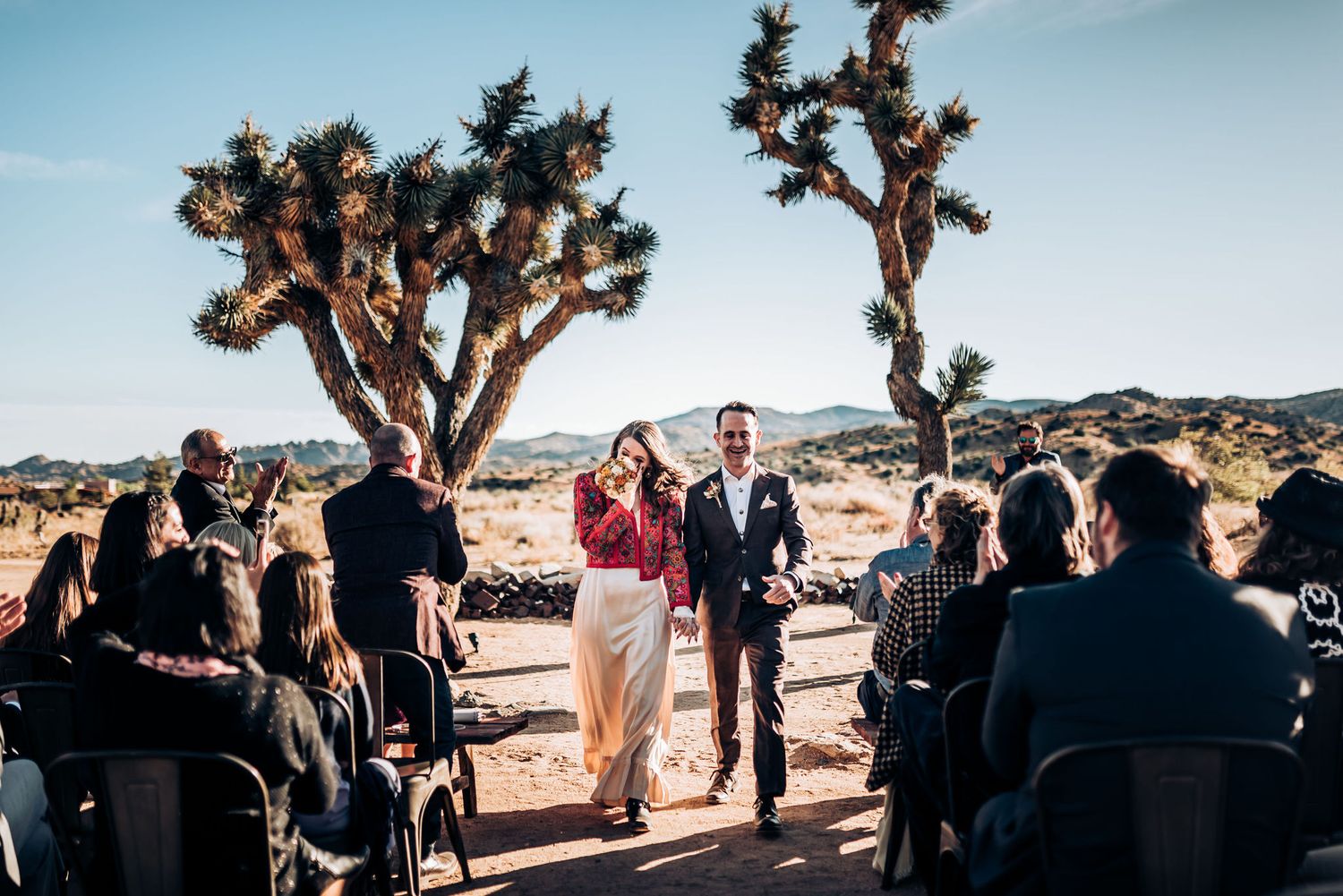 Guests seated in rows watch desert wedding ceremony beneath towering Joshua Trees.