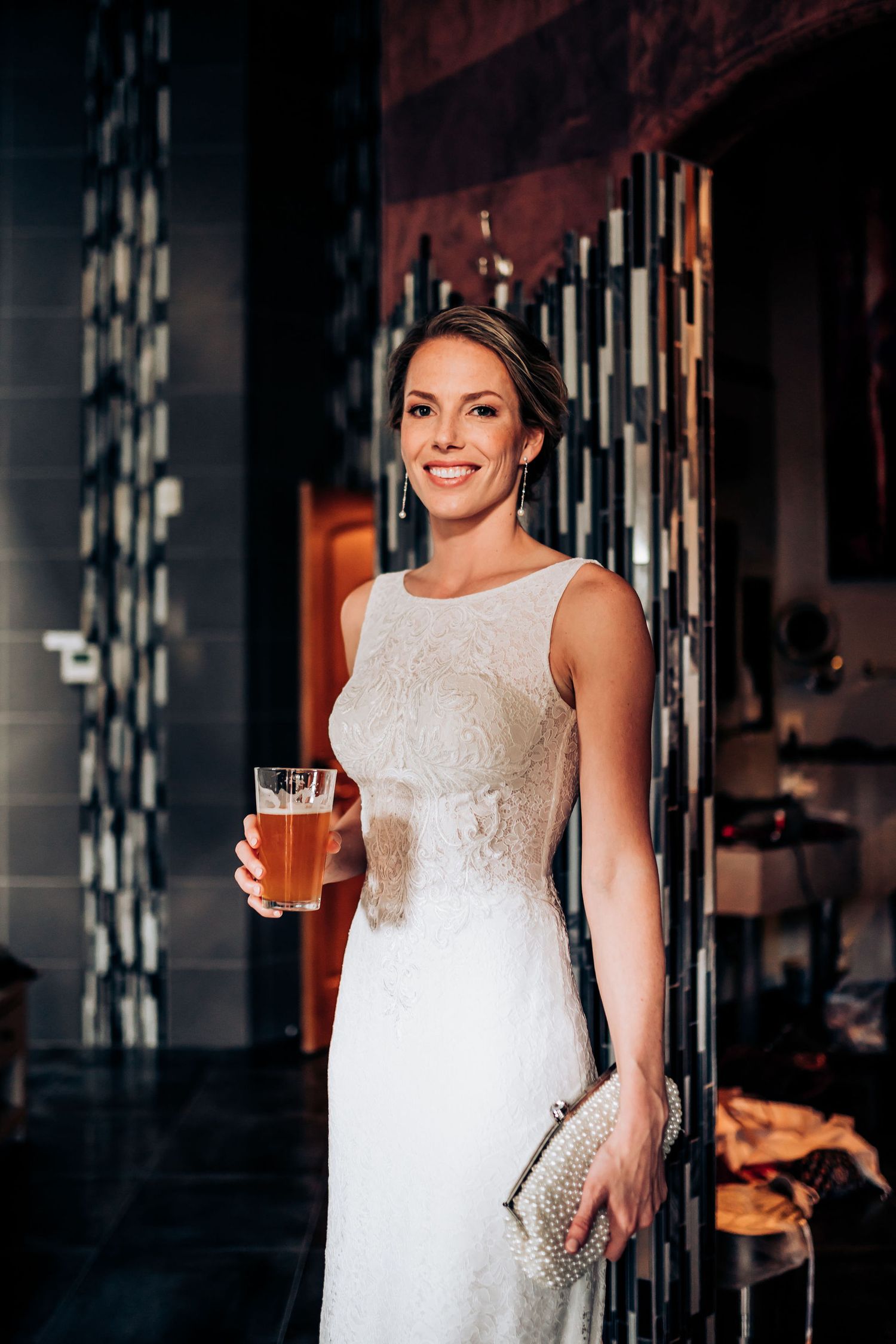 Person in white beaded wedding dress holding a cocktail in an elegant venue.