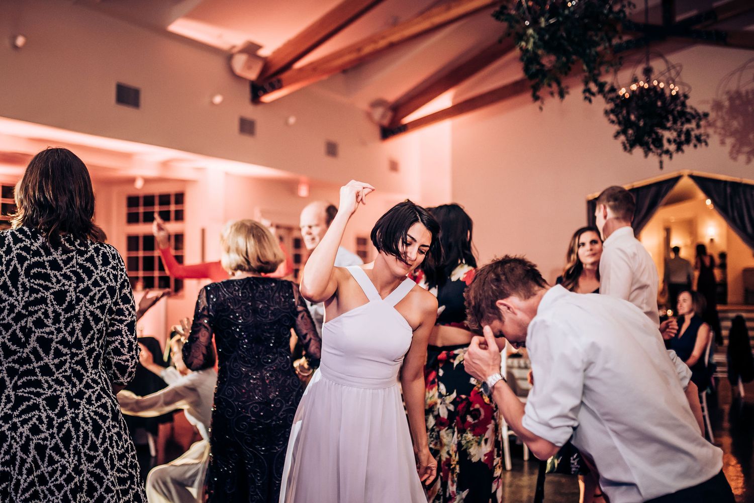 Wedding guests dancing and celebrating on a lively dance floor illuminated with pink lighting.