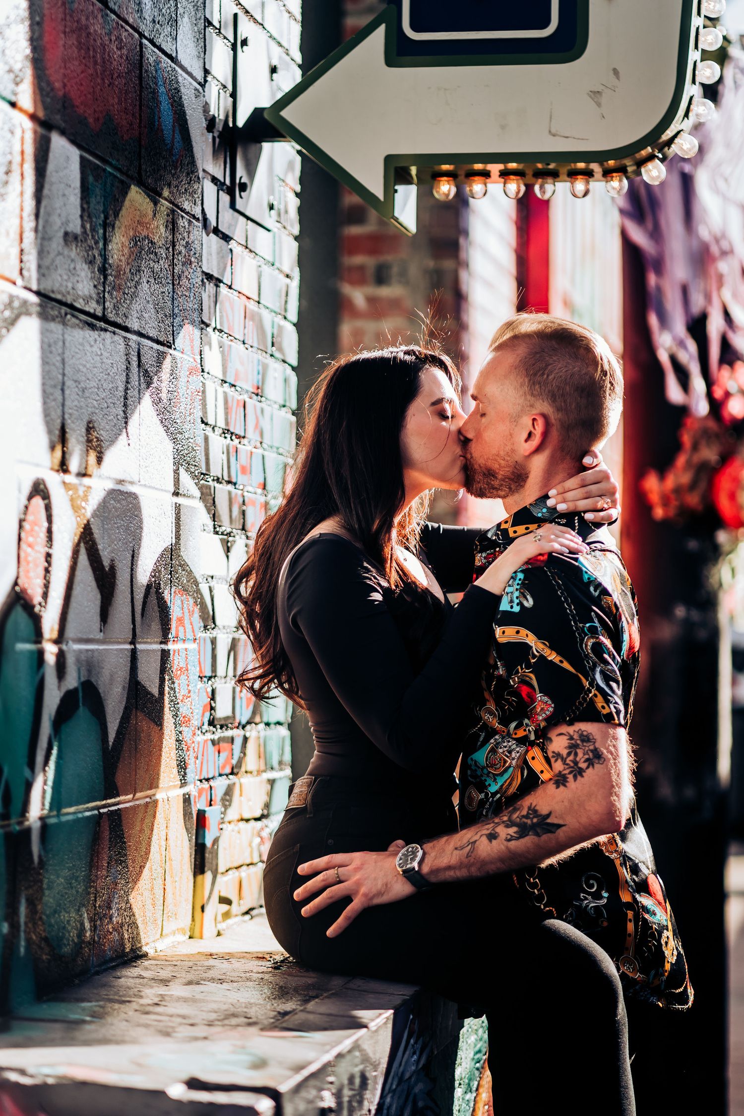 A couple embracing against a graffiti wall in an urban alley.