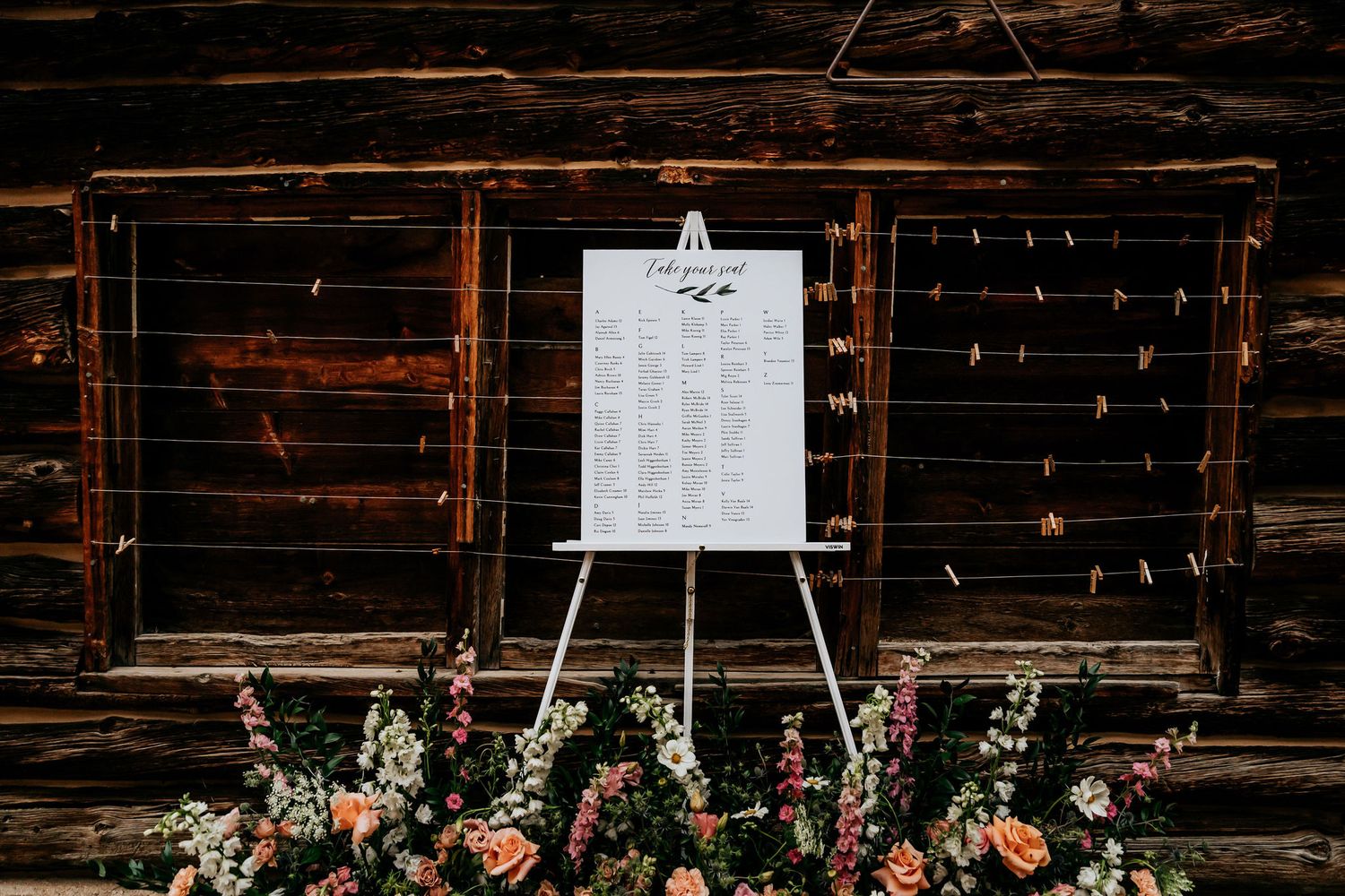 Wedding seating chart display with floral arrangements against rustic wooden barn wall.