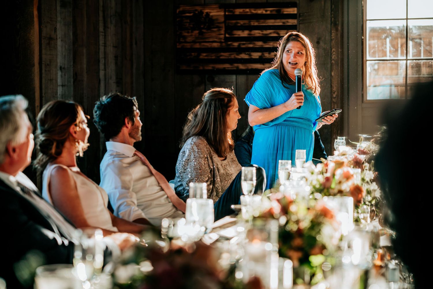 A speaker delivers a toast during a wedding reception while guests listen at elegantly decorated tables.