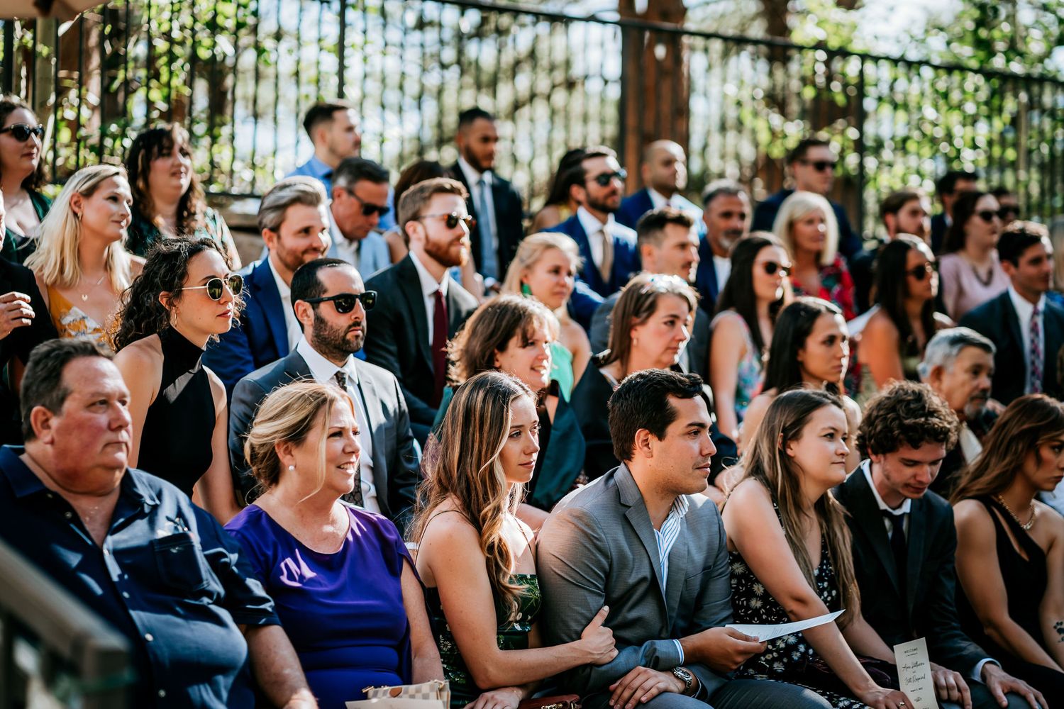 Wedding guests seated outdoors watching the ceremony in formal attire.