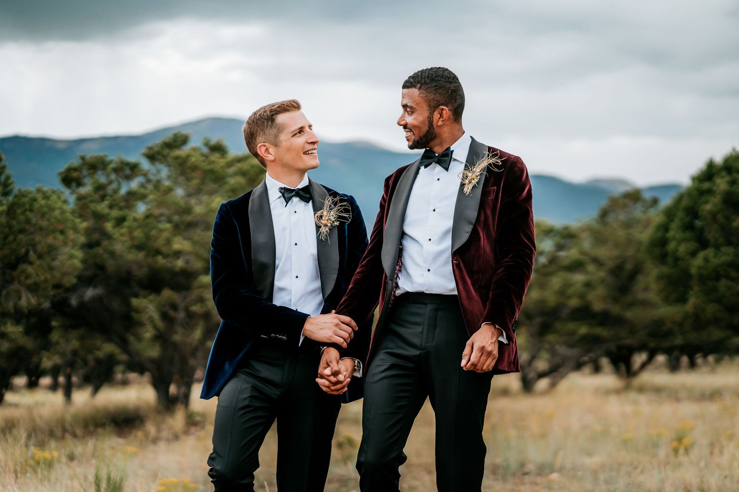Two people in formal attire sharing a laugh in mountain field setting.