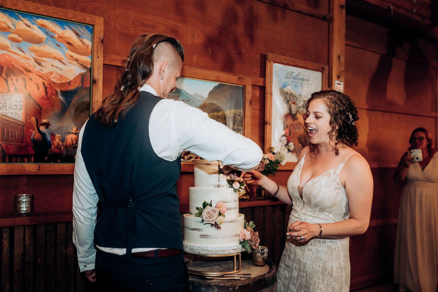 Wedding couple performs cake cutting ceremony at rustic indoor reception.