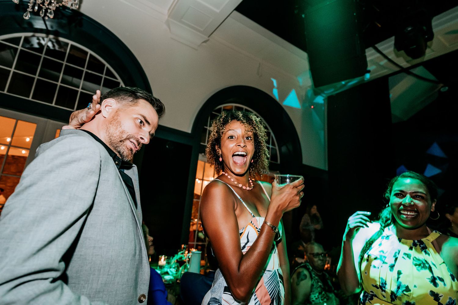 Candid moment of guests laughing and dancing at reception with dramatic colored lighting.