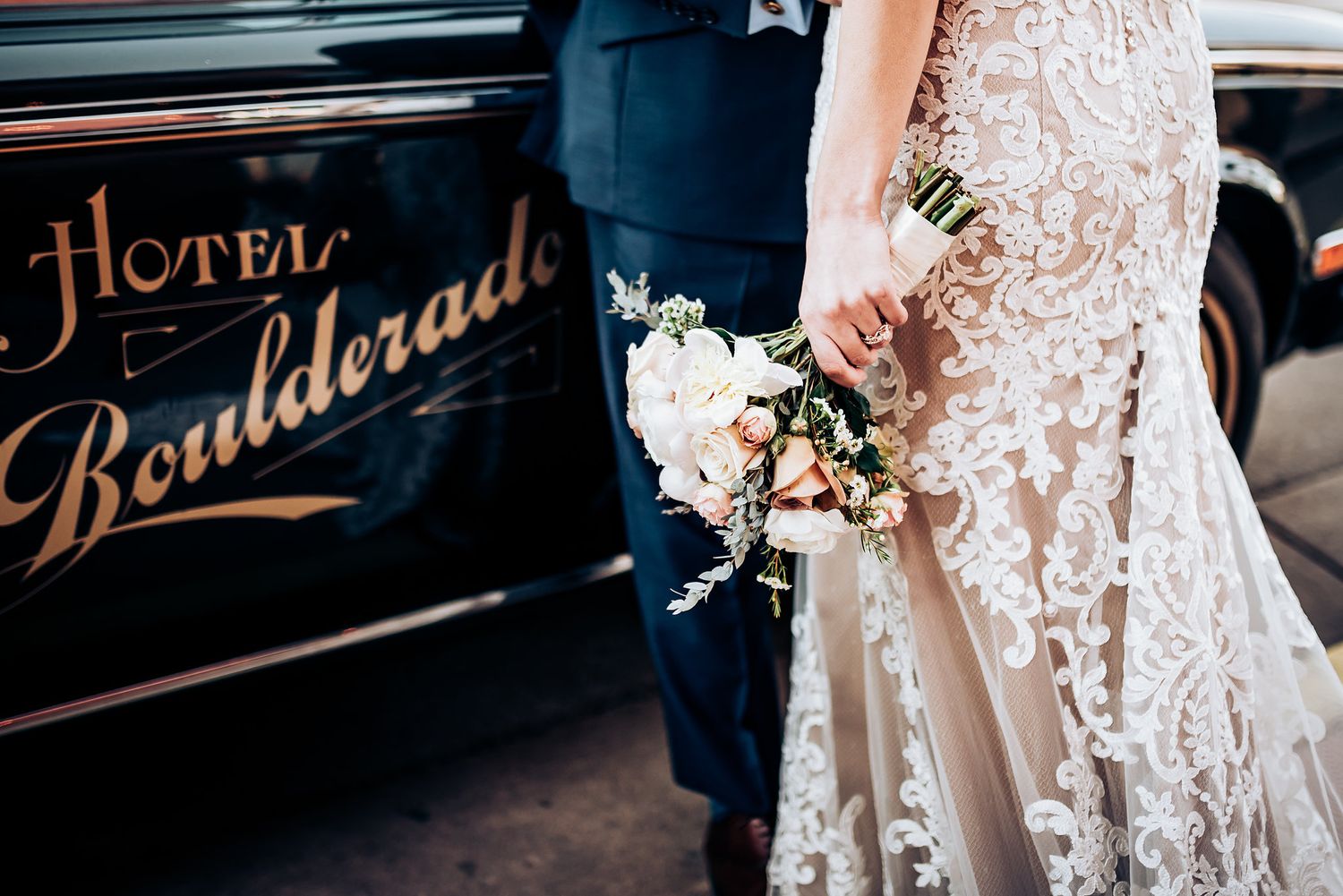 Elegant couple stands beside vintage Hotel Boulevarde sign with lace wedding dress detail.
