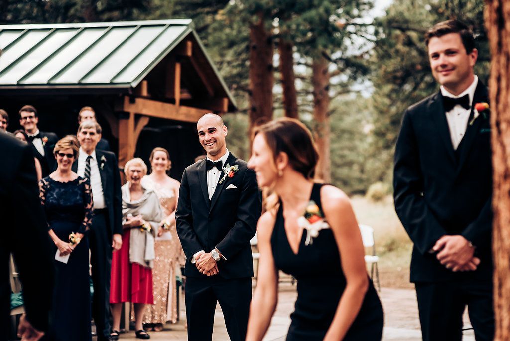 Wedding party and guests gathered outside rustic wooden pavilion.