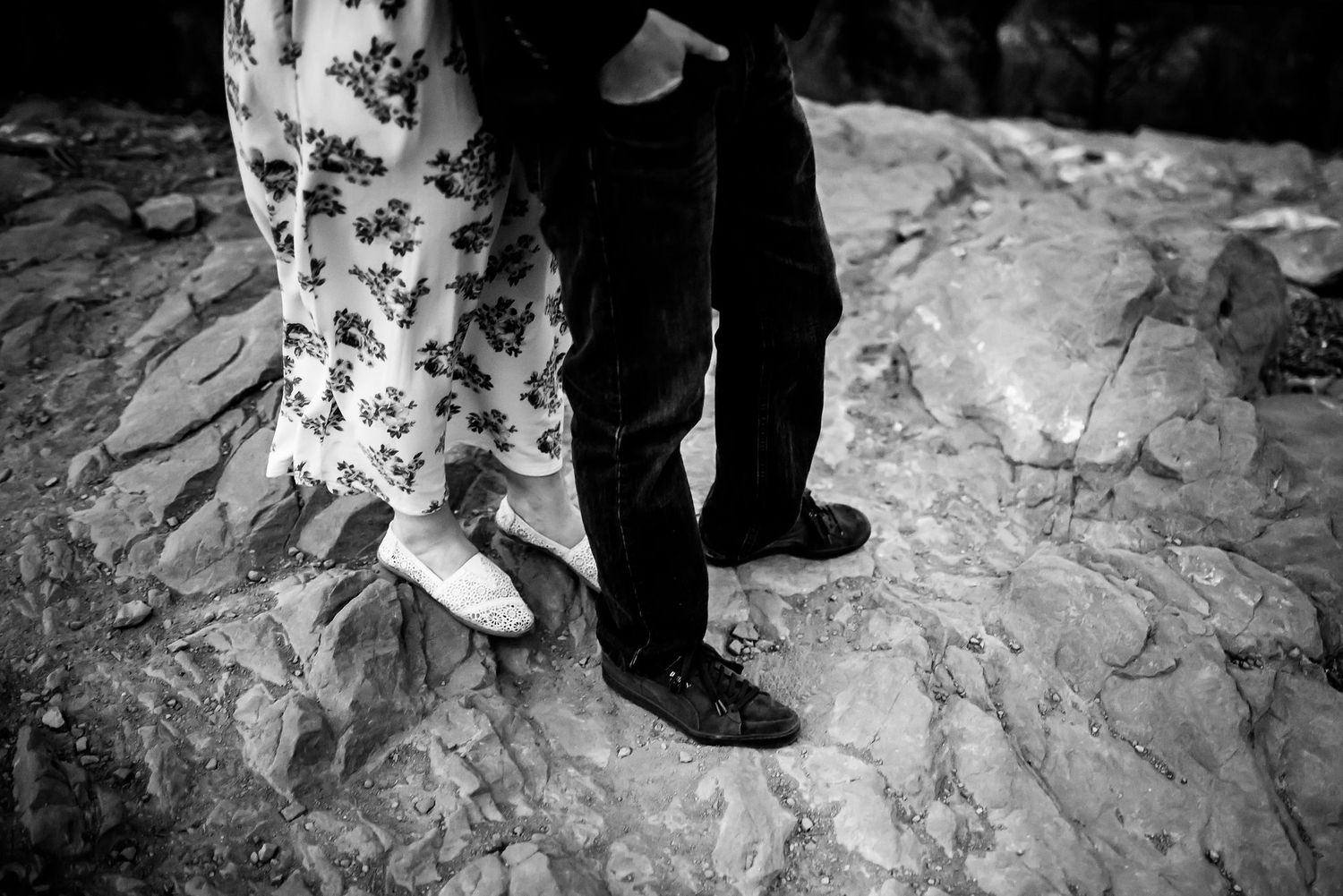 Black and white detail shot of couple's feet standing on rocky mountain terrain.