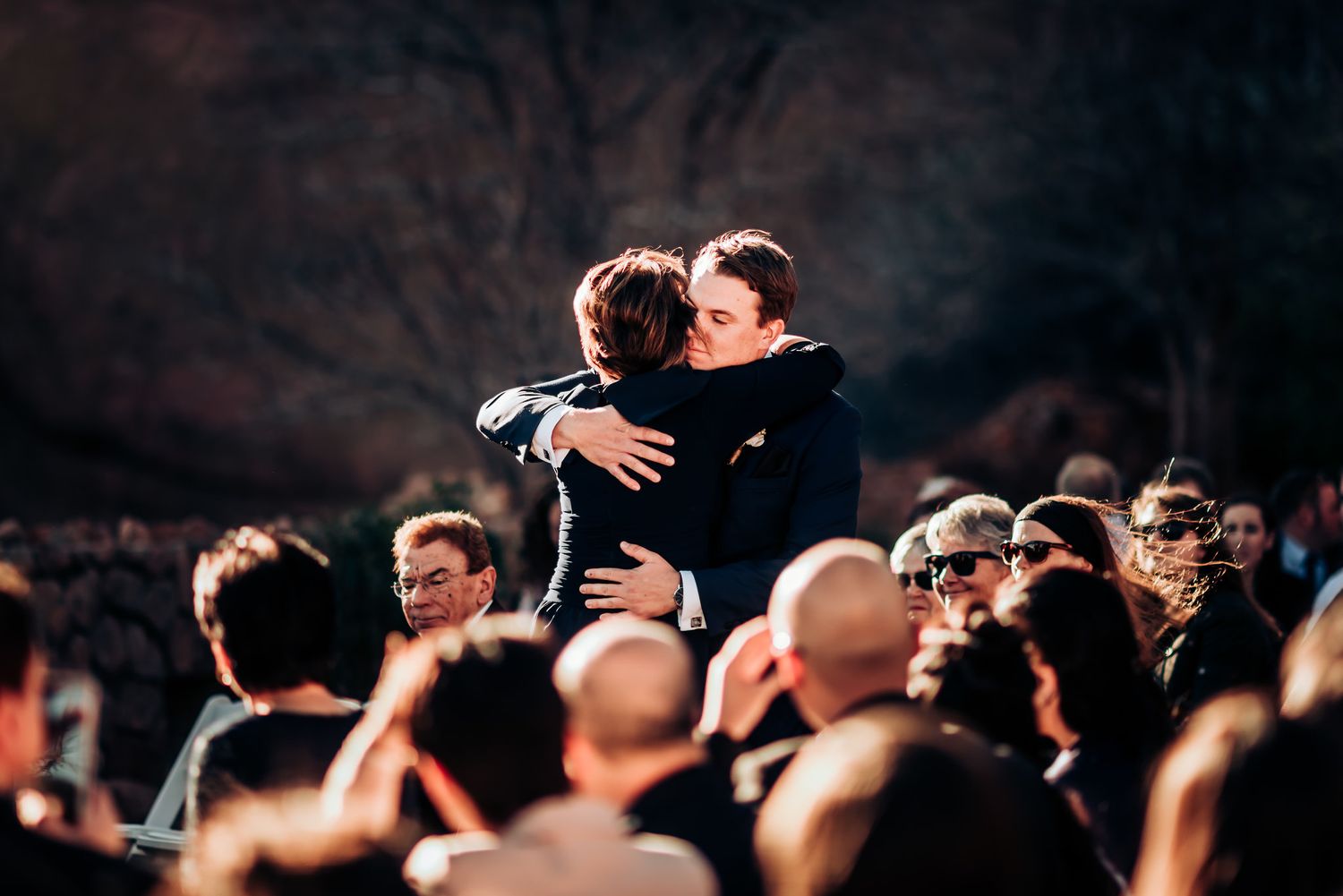 An emotional embrace captured during a wedding ceremony with crowd in background.