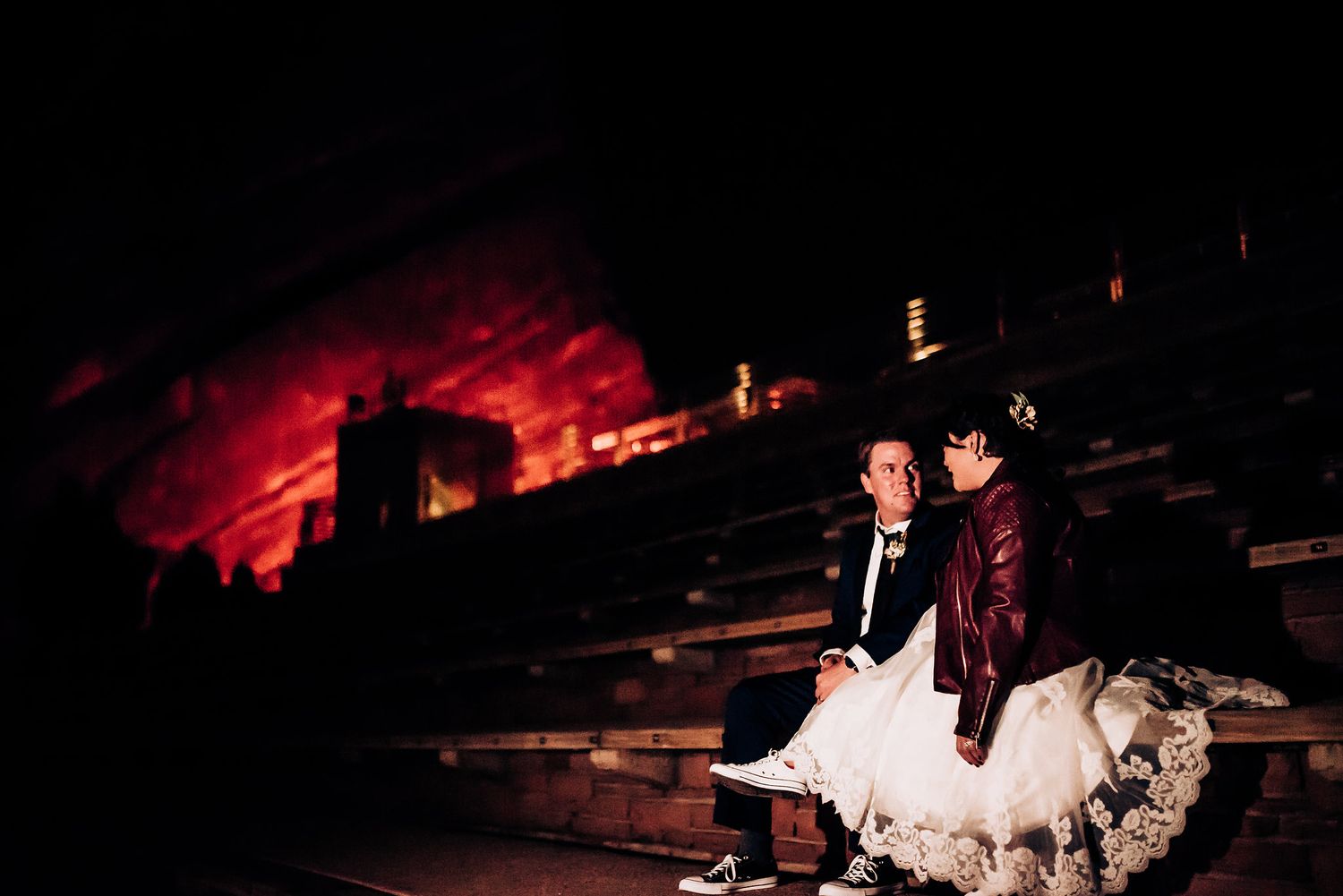 Couple sitting on steps against dramatic red-lit backdrop at nighttime.
