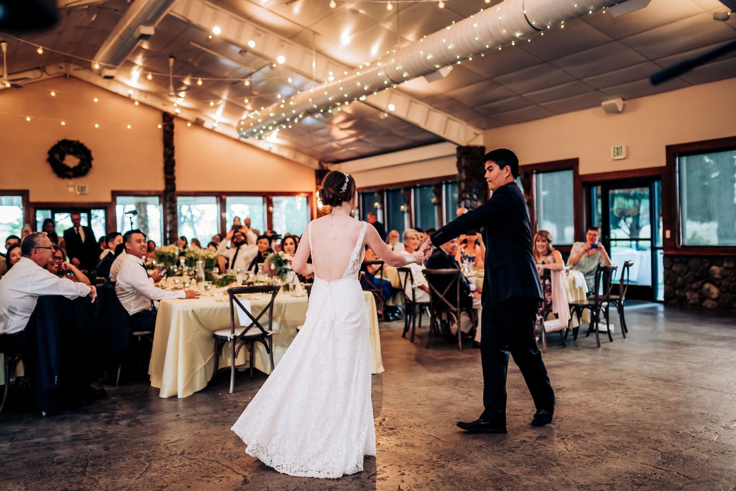 Wedding reception scene with string lights overhead and guests seated at round tables.