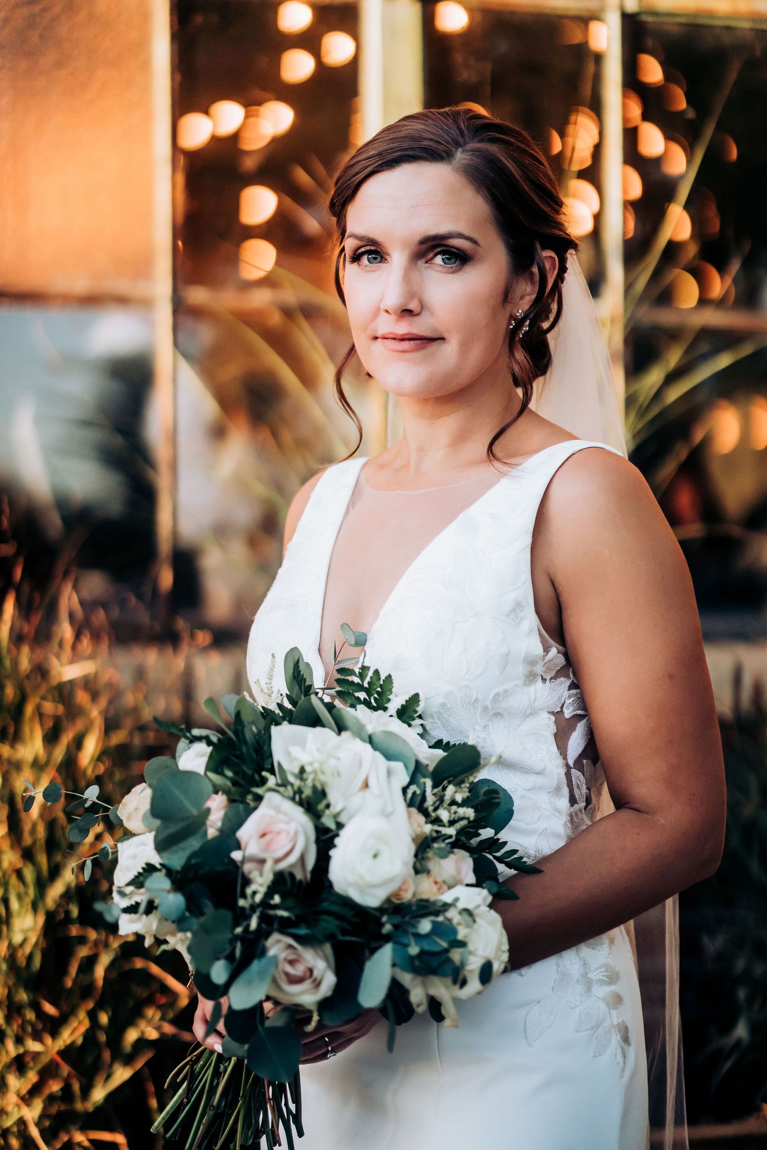Bride holding white and green bouquet in elegant sleeveless wedding dress.