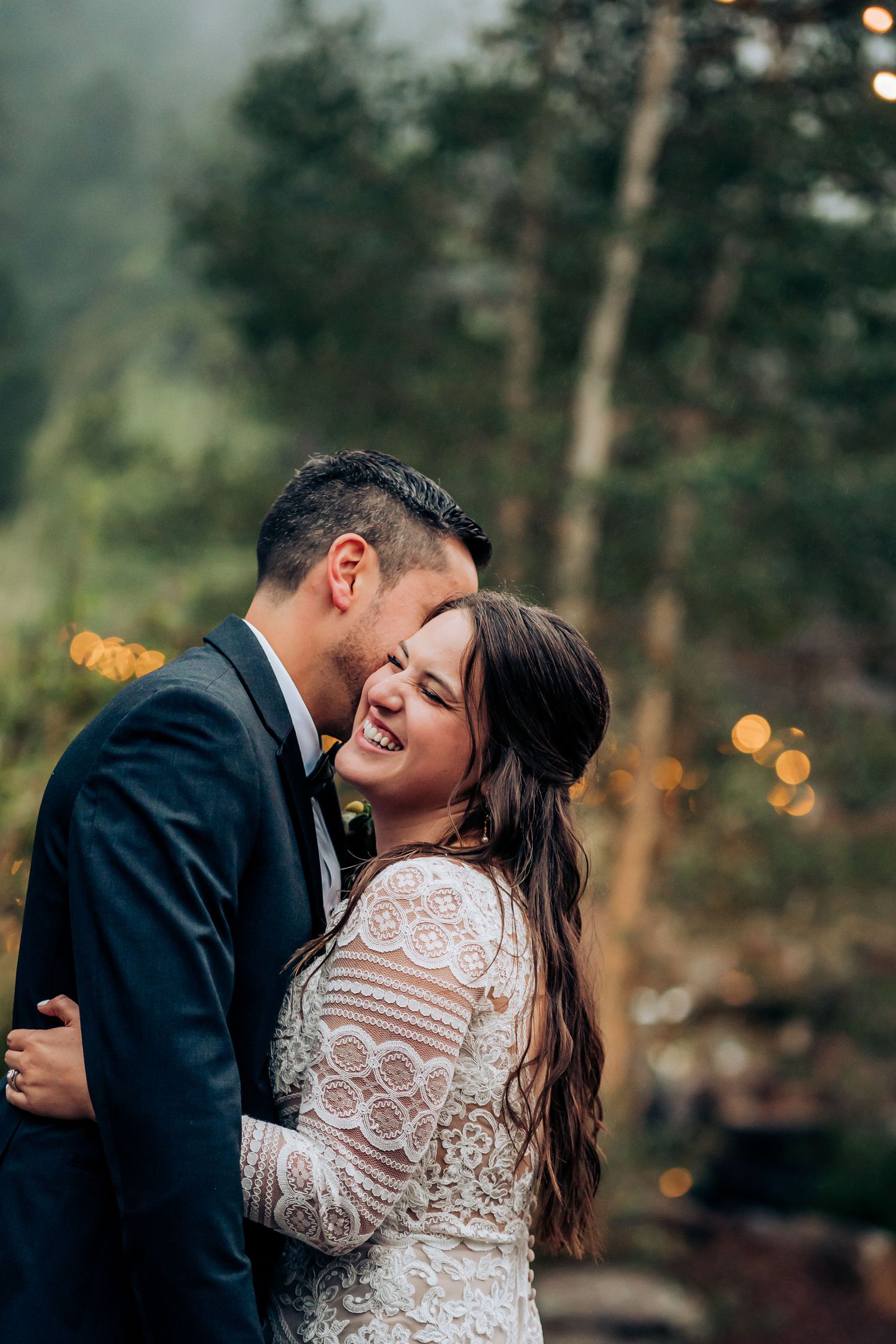 Intimate moment shared between newlyweds with string lights glowing in forest background.