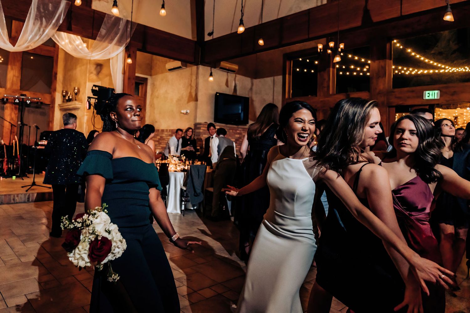 Wedding reception guests dancing and celebrating in an elegantly lit indoor venue.