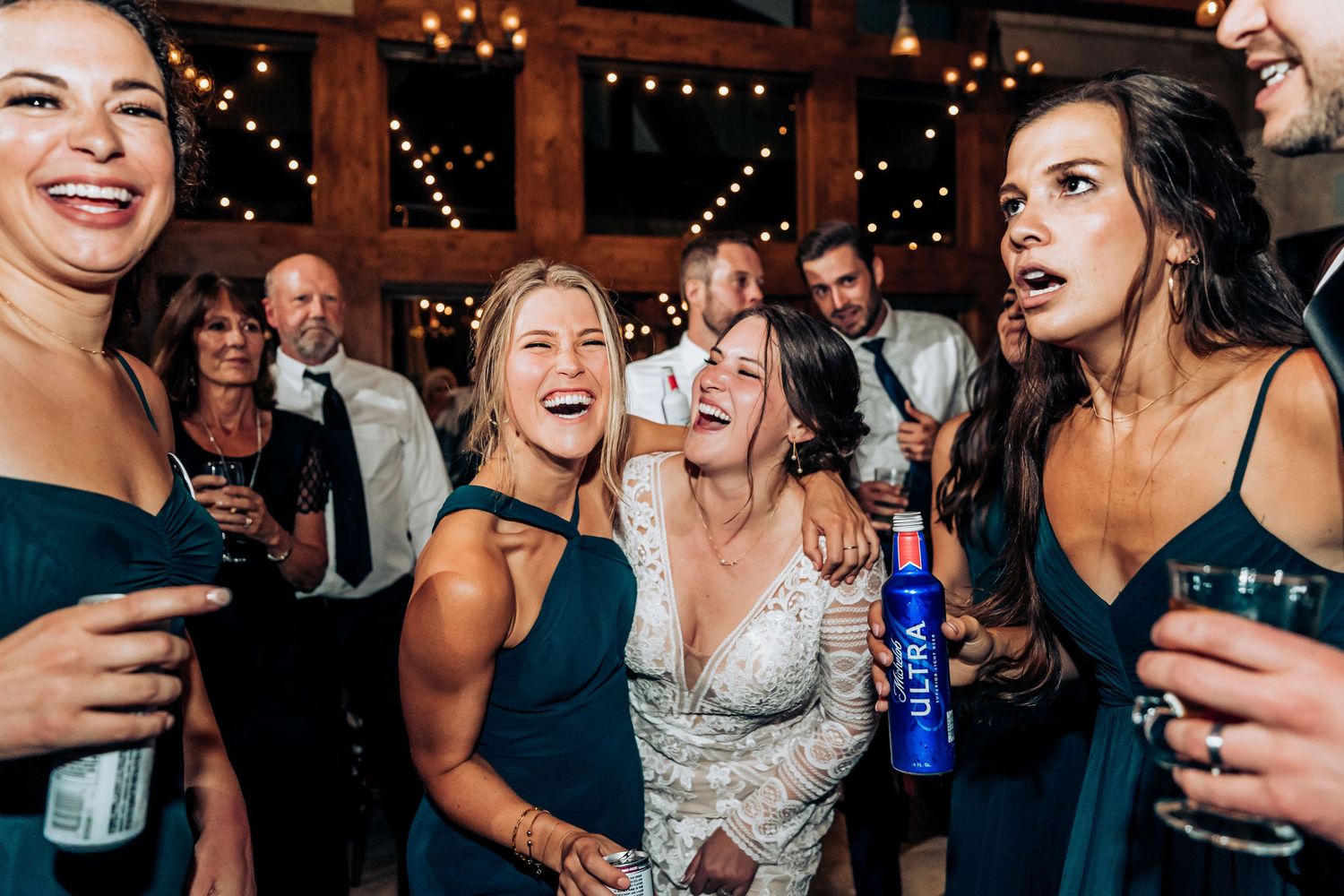 Wedding party celebrating joyfully with drinks on a lively dance floor under string lights.