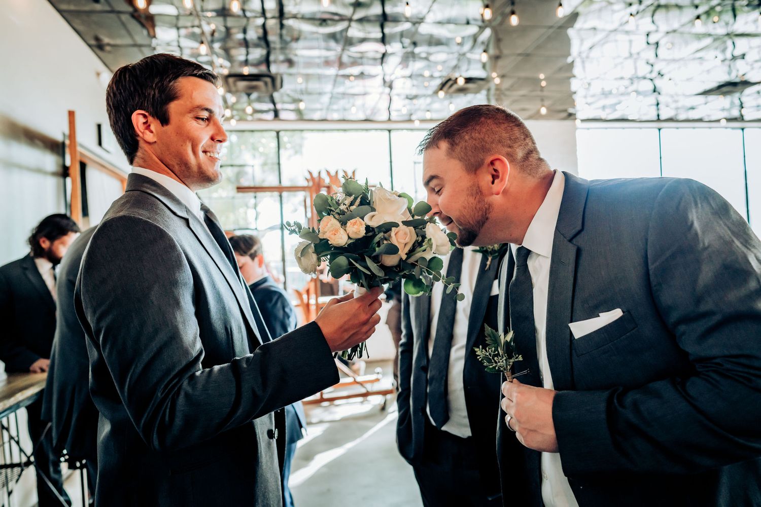 Two people in formal attire sharing a humorous moment with a bouquet.