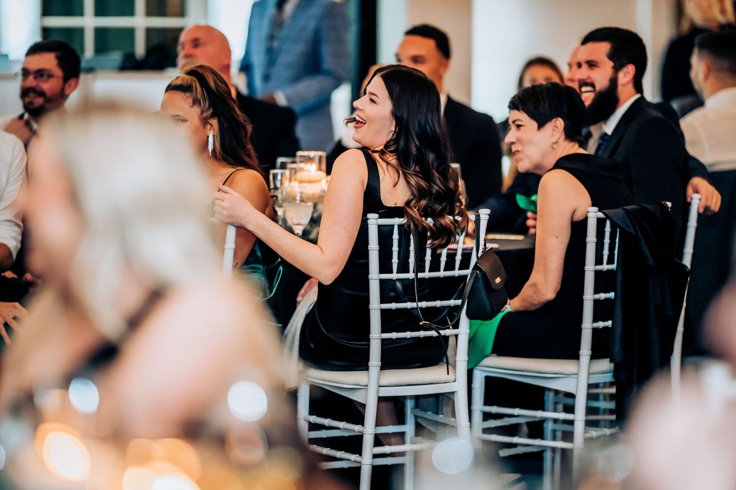 Guests in formal attire seated at chiavari chairs during wedding reception.