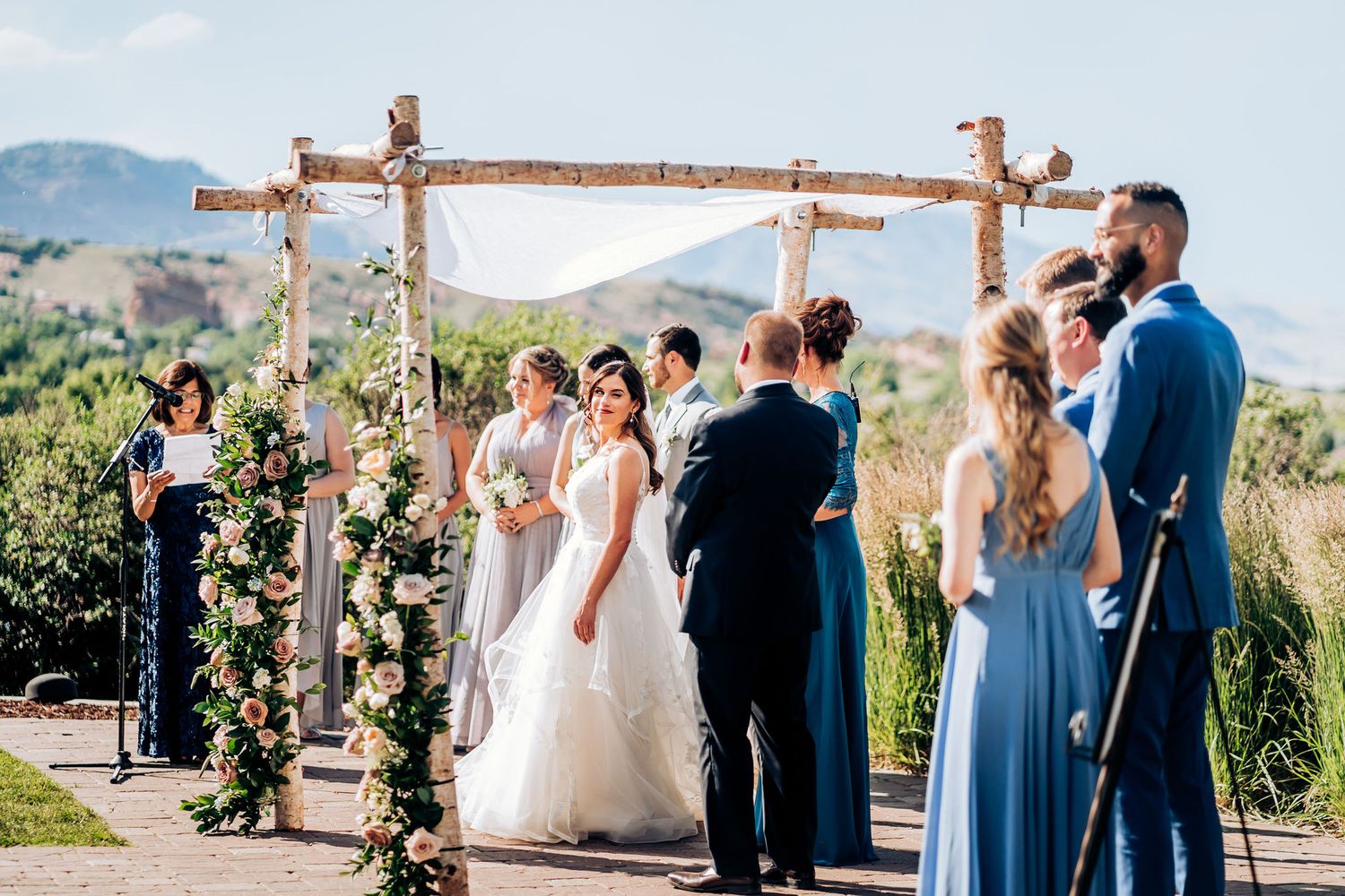Elegant mountain wedding ceremony under wooden arch with flowing white fabric and flowers.