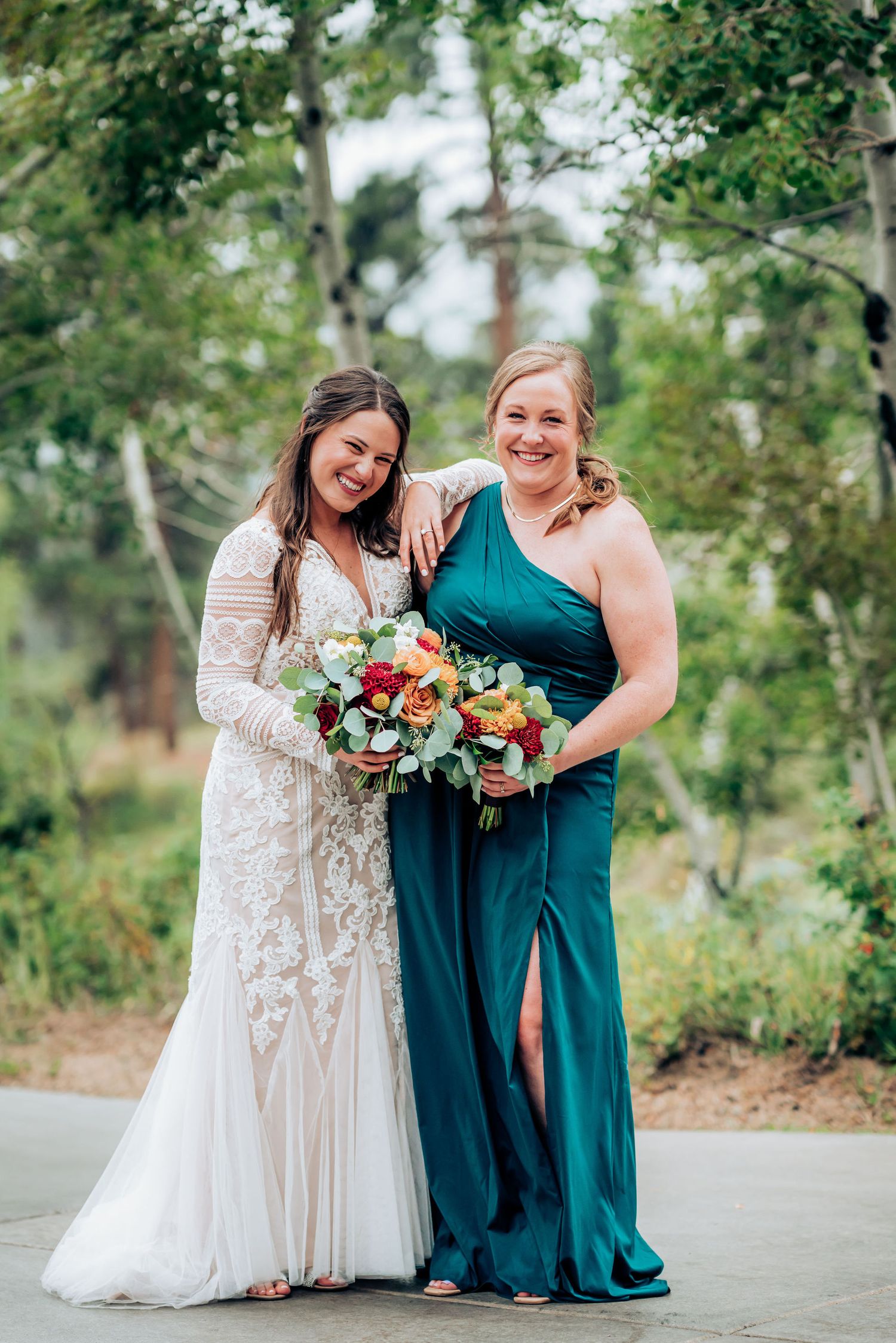 Wedding party members in white lace and teal dresses pose with colorful bouquets in an outdoor garden setting.