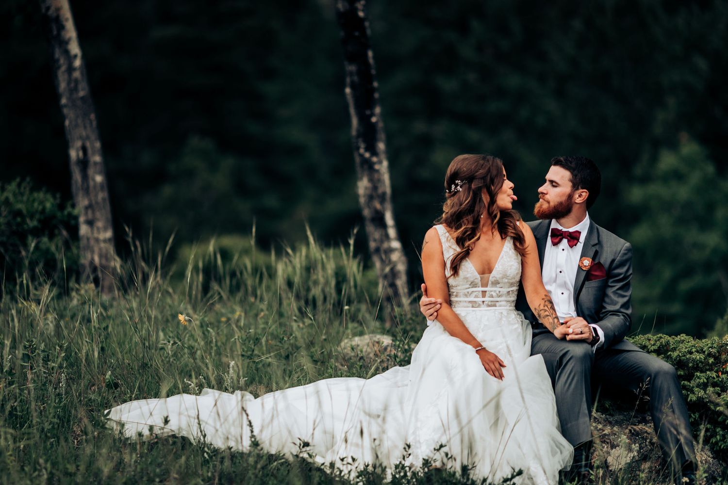 Wedding couple sitting together on a rock in a serene mountain meadow with forest backdrop.