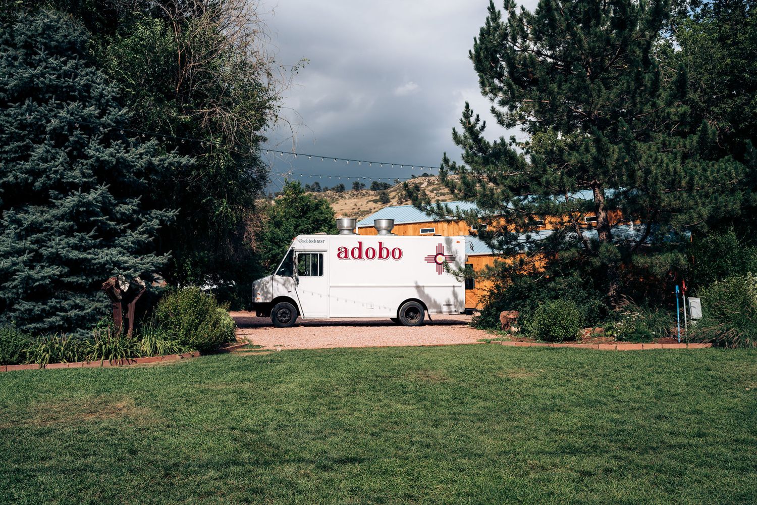 White food truck parked on grass with mountains and evergreen trees in the background.