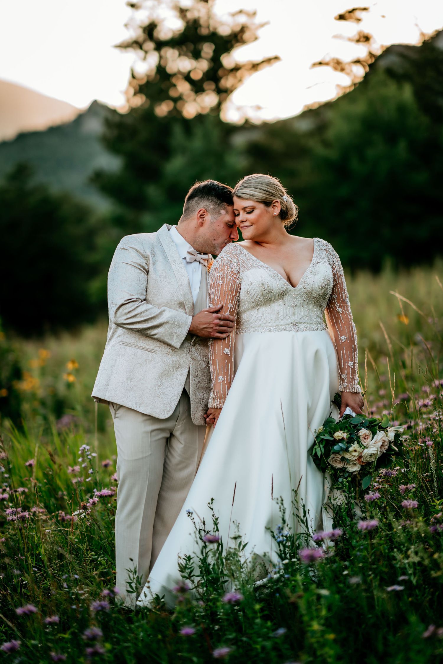 Intimate wedding portrait in wildflower field with mountain sunset backdrop.