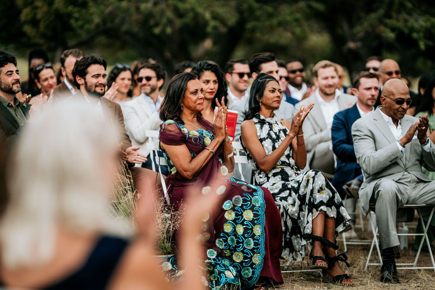 Wedding guests react emotionally while watching ceremony in outdoor setting.