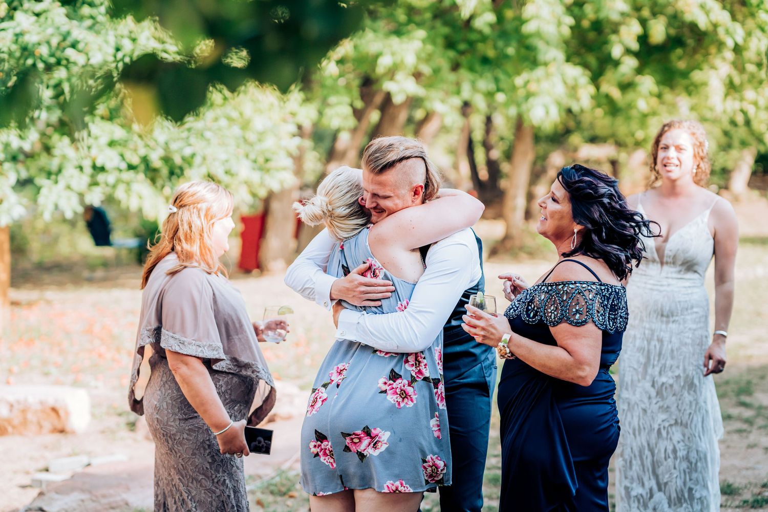 Wedding guests share emotional embraces during an outdoor celebration.