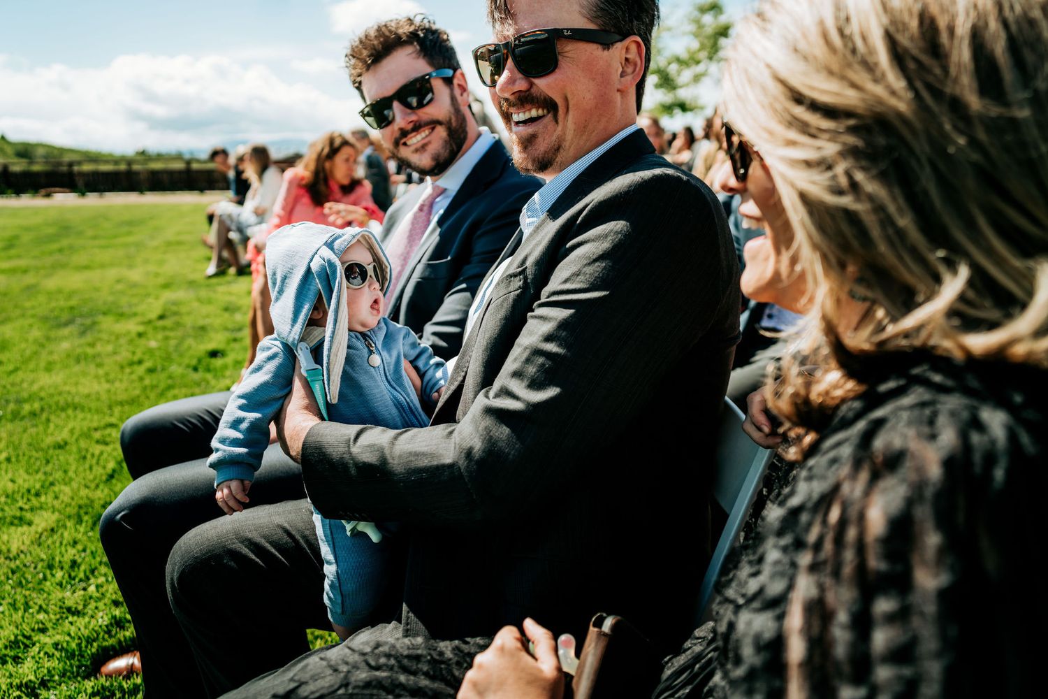 Wedding guests laugh and smile while enjoying an outdoor ceremony.