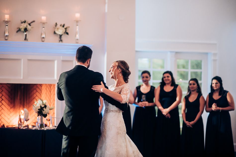 Wedding couple shares their first dance while bridesmaids in black dresses watch from the side.