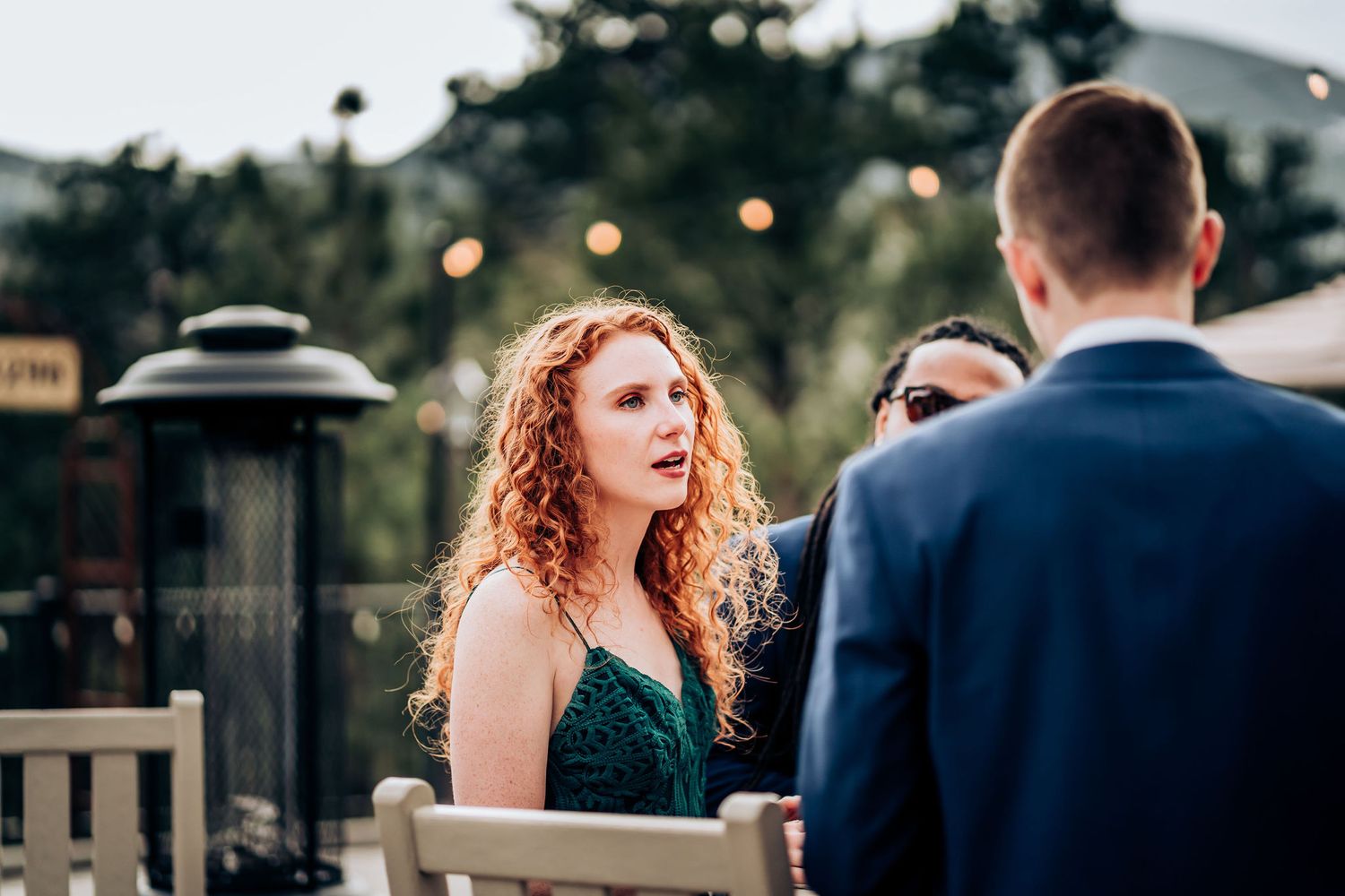 A guest in an emerald dress converses during an outdoor evening reception.