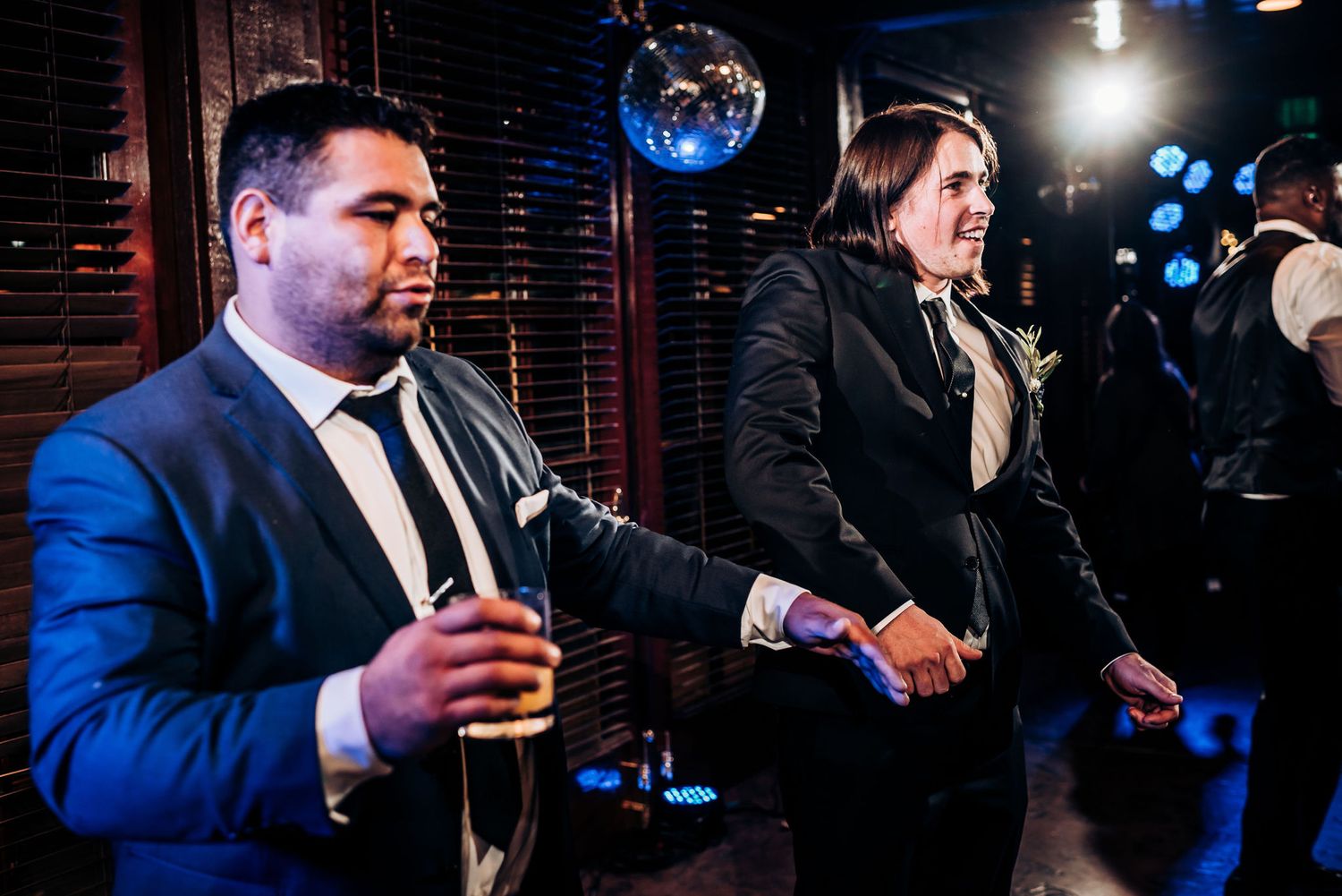 Wedding guests enjoying drinks and dancing under a disco ball at a dimly lit venue.