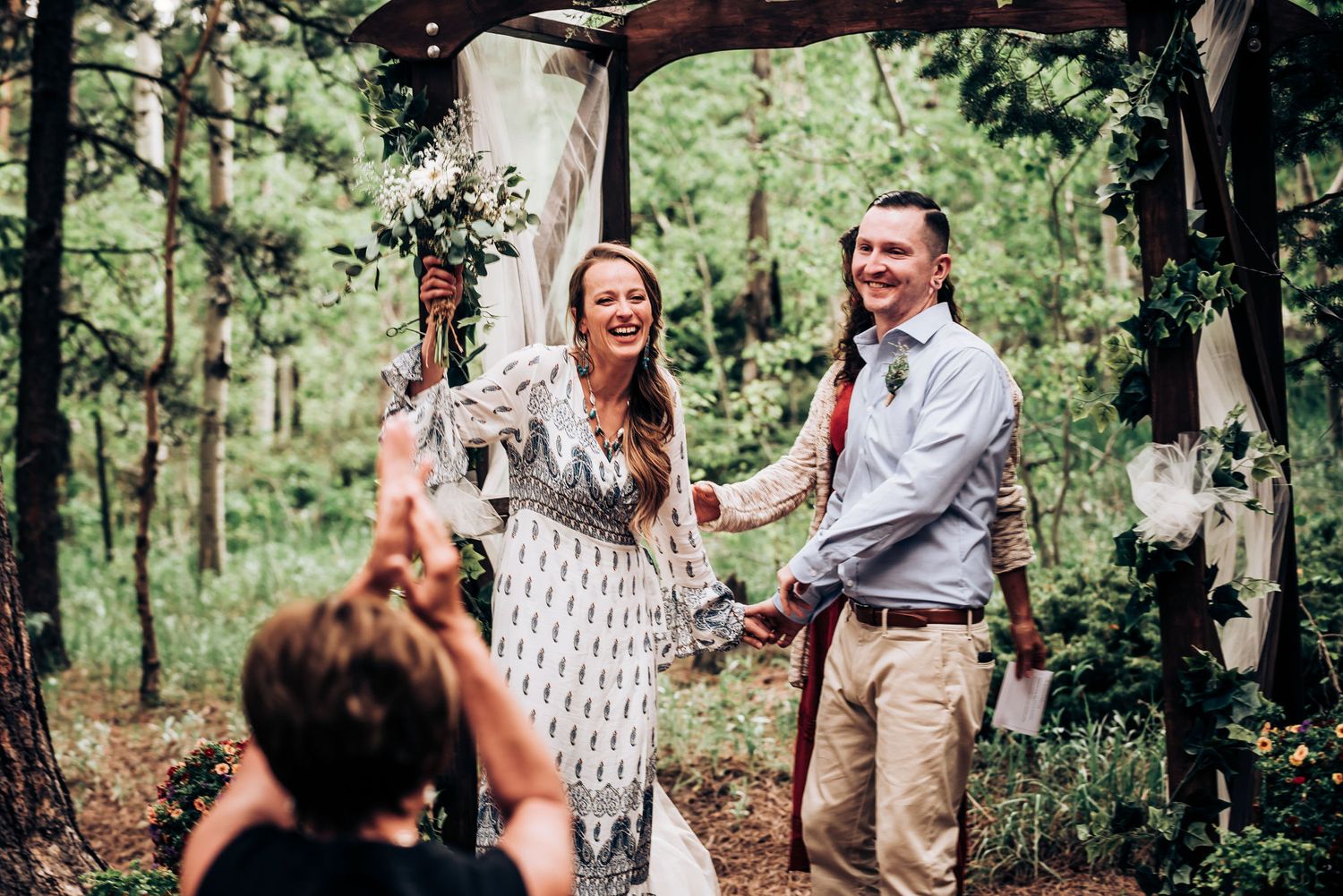 A joyous celebration moment during a forest wedding ceremony under a decorated wooden arch.