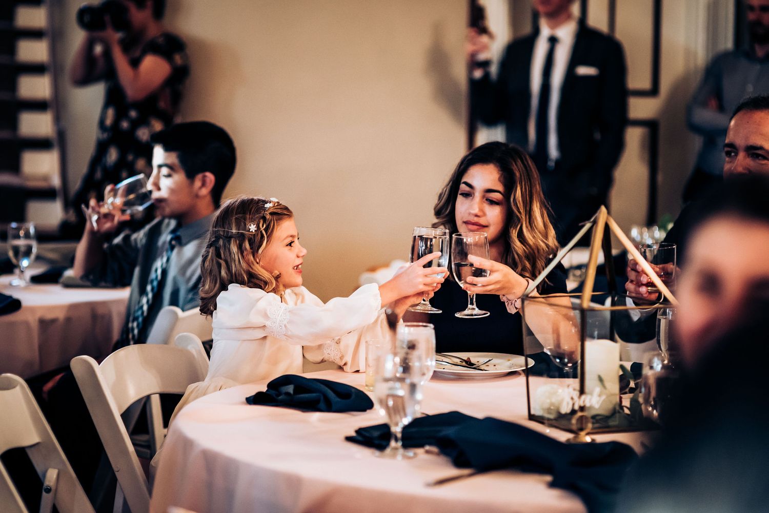 Guests dining at an elegant table setting during a formal event with wine glasses and table decorations.