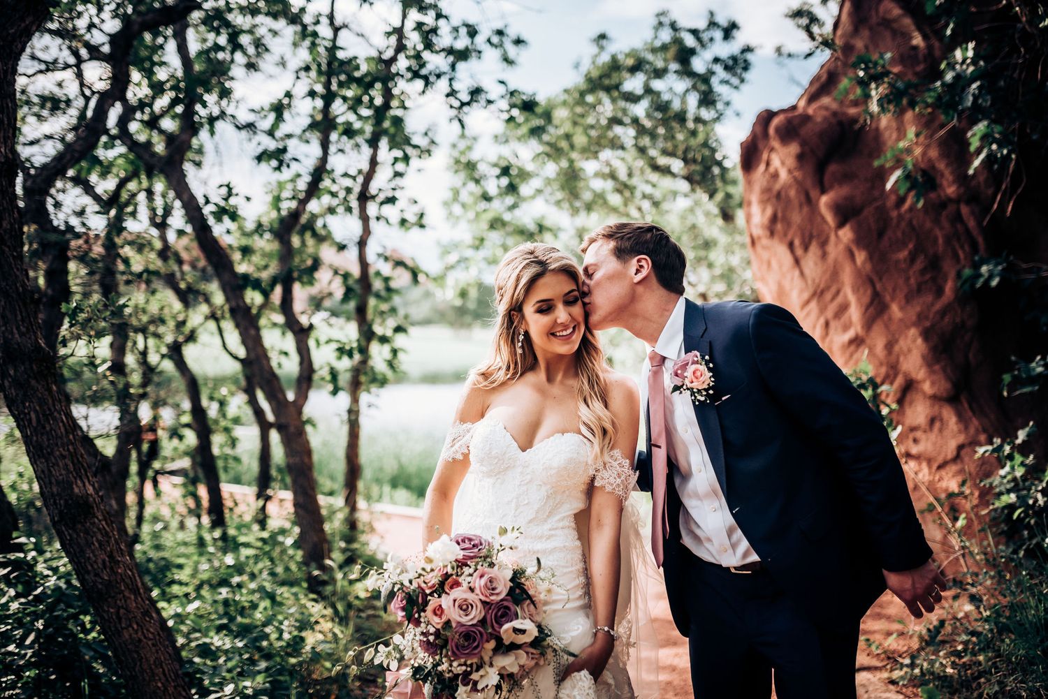 Romantic wedding photo amongst trees with red rock formations and pink floral bouquet.