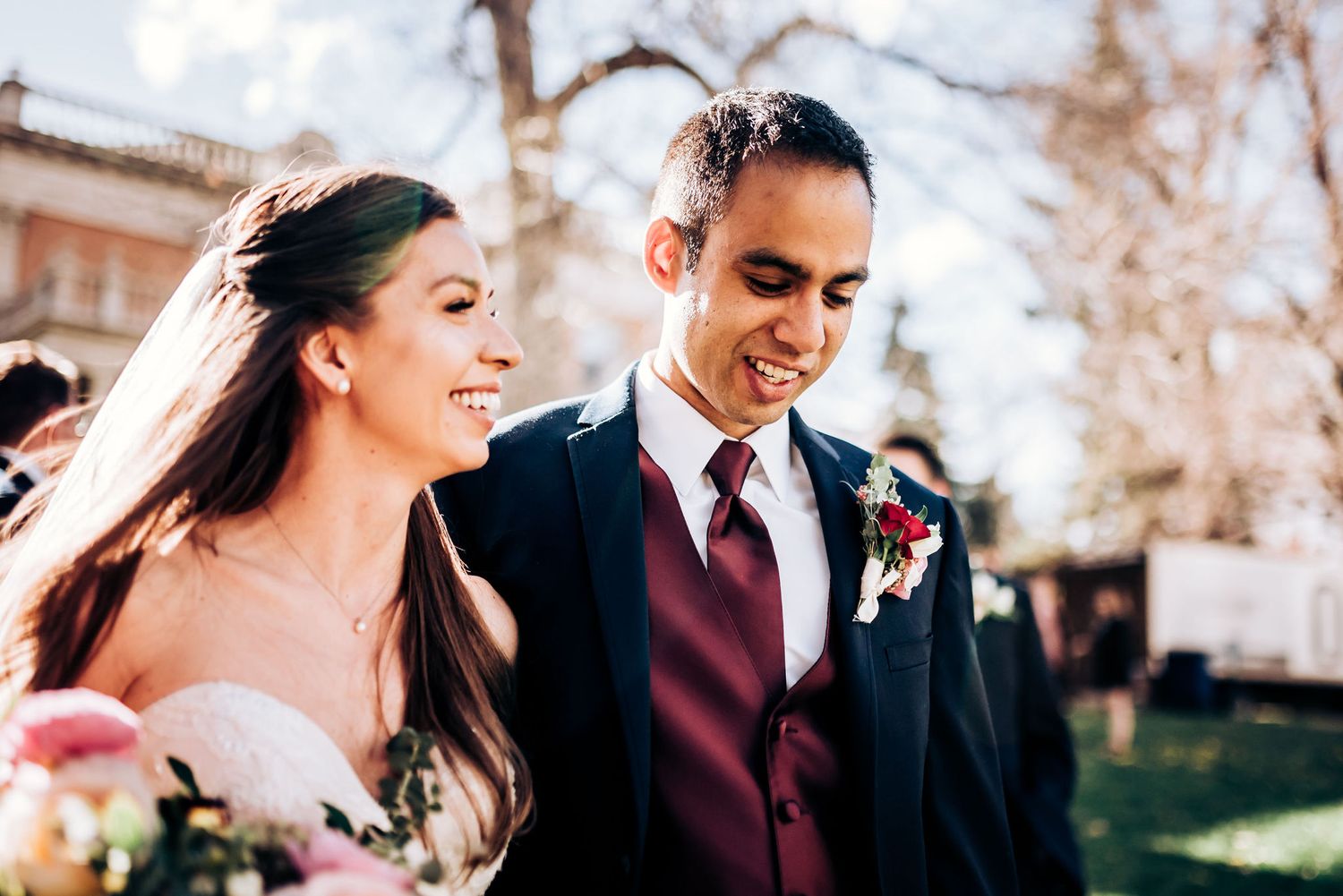 Candid moment between couple in formal wedding attire outside on sunny day.