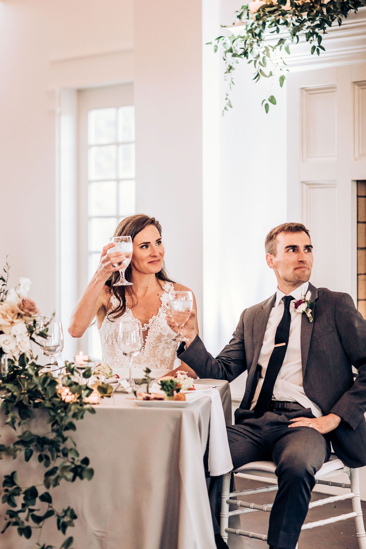 A couple sits at their sweetheart table during wedding reception toasts.