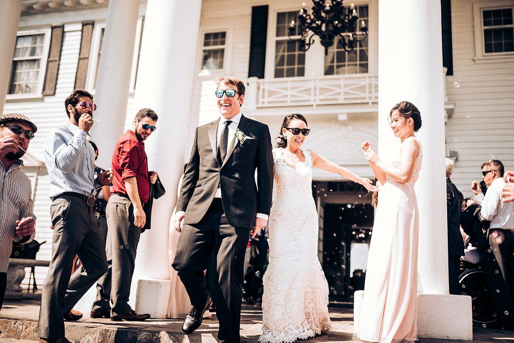 Wedding party celebrating with confetti outside a white columned building on a sunny day.