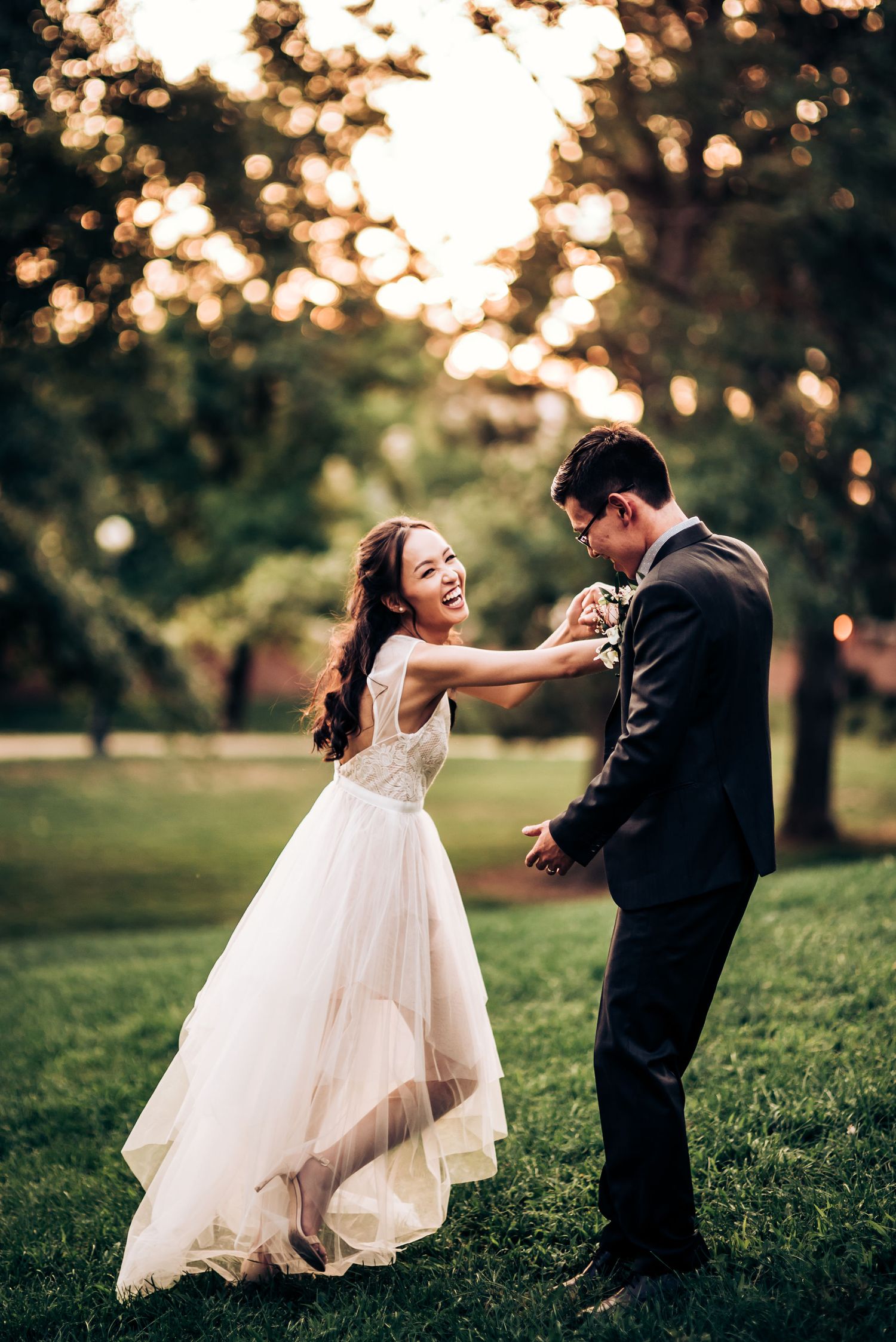 A couple dances playfully on a lawn with golden sunset bokeh in the background.