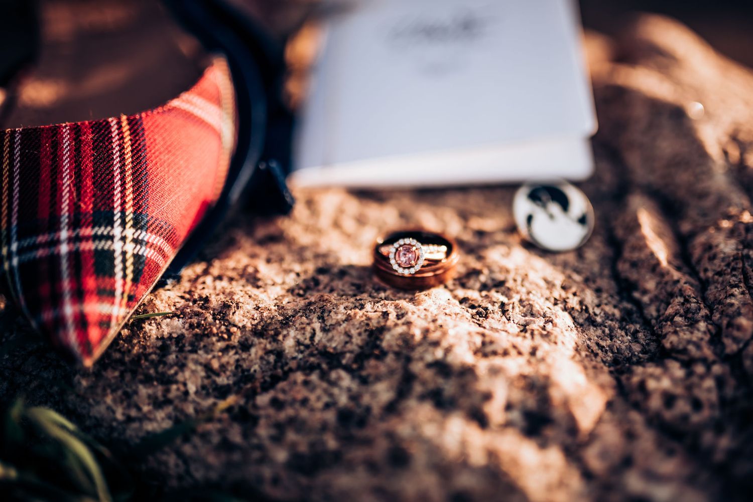 A diamond engagement ring nestled among plaid accessories on a textured surface.
