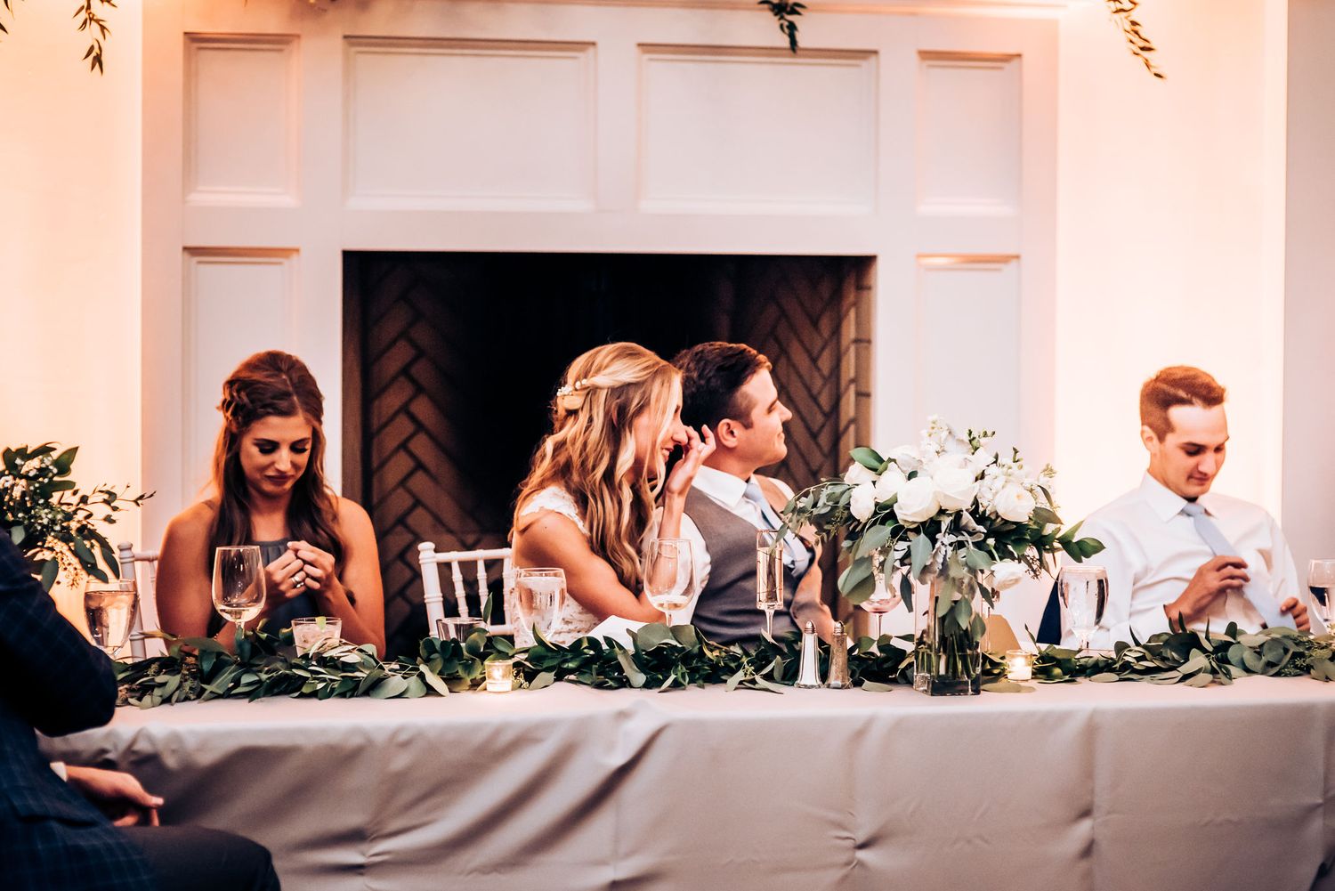 Wedding reception head table moment with elegant floral decorations and white linens.