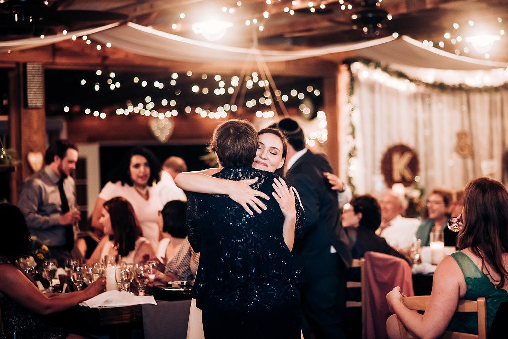Guests embrace during emotional moment at wedding reception with twinkle lights overhead.
